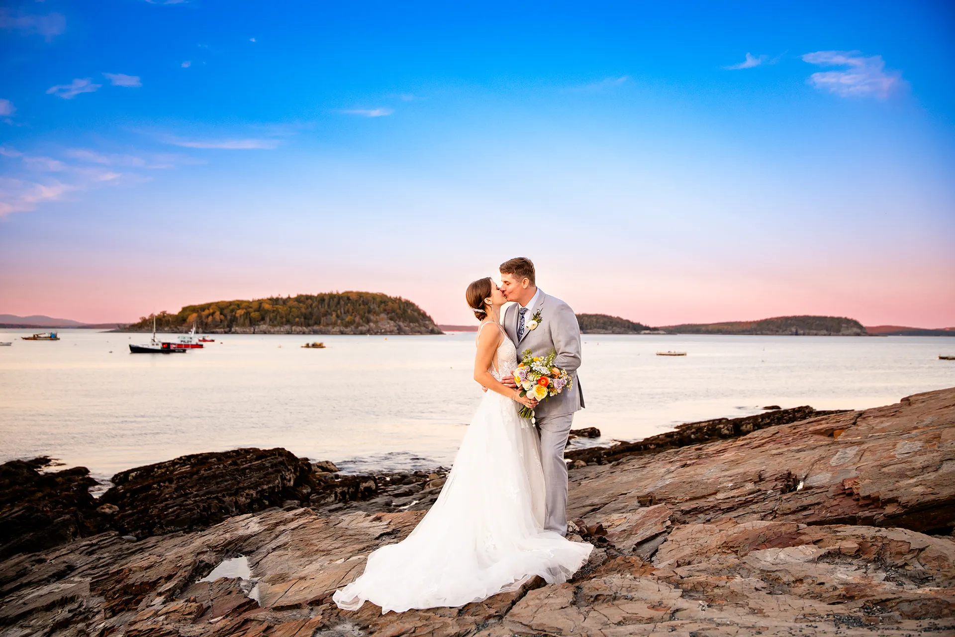 A bride and groom kiss at sunset in front of Frenchman Bay during their wedding portraits at the Bar Harbor Inn and Spa in Maine.