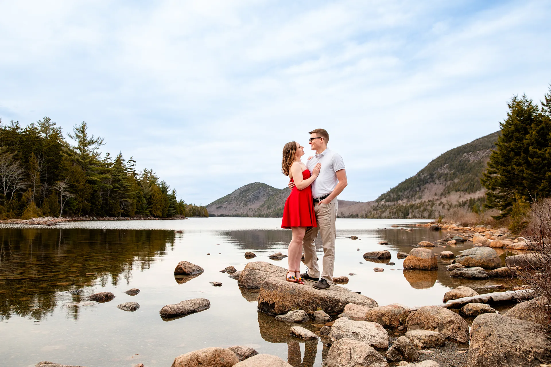maine engagement photography chelsea mike 05 An engaged couple stand on a rock and smile at each other during an engagement session at Jordan Pond in Acadia National Park, Maine.
