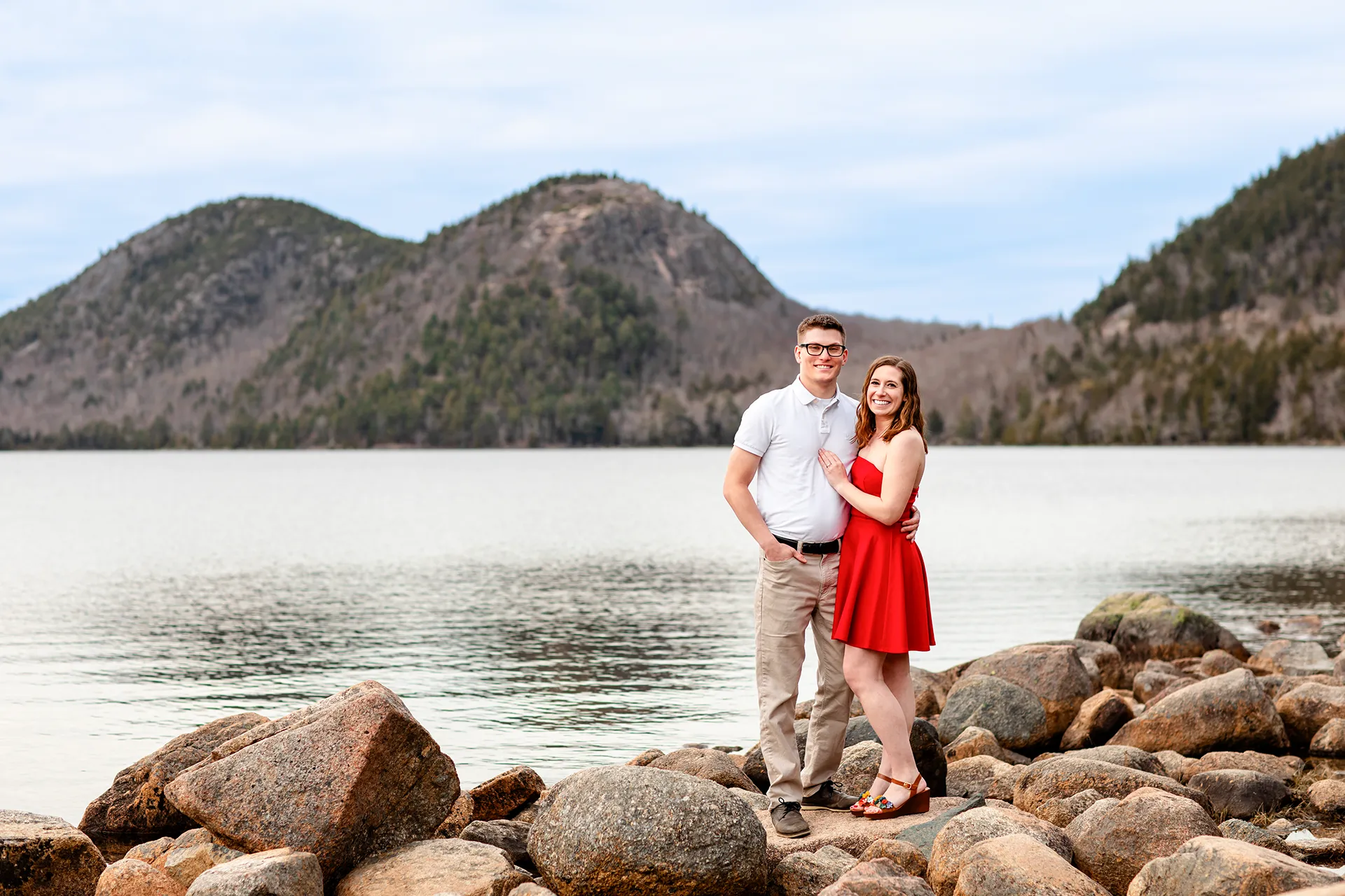 maine engagement photography chelsea mike 07 An engaged couple smile and pose on a rock during an engagement session at Jordan Pond in Acadia National Park, Maine.
