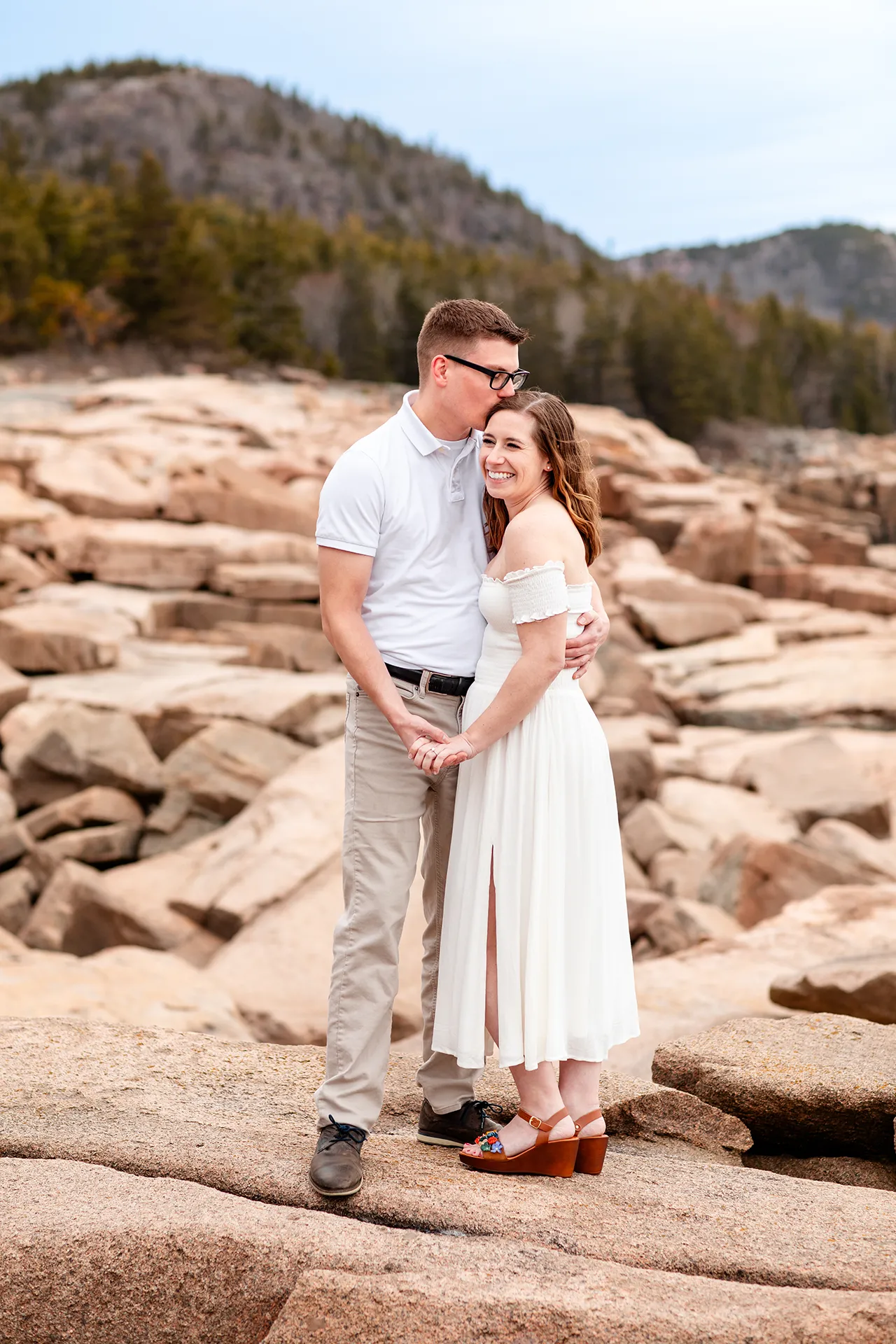 maine engagement photography chelsea mike 12 A woman laughs as a man kisses her on the head during an engagement session near the Ocean Path in Acadia National Park, Maine.
