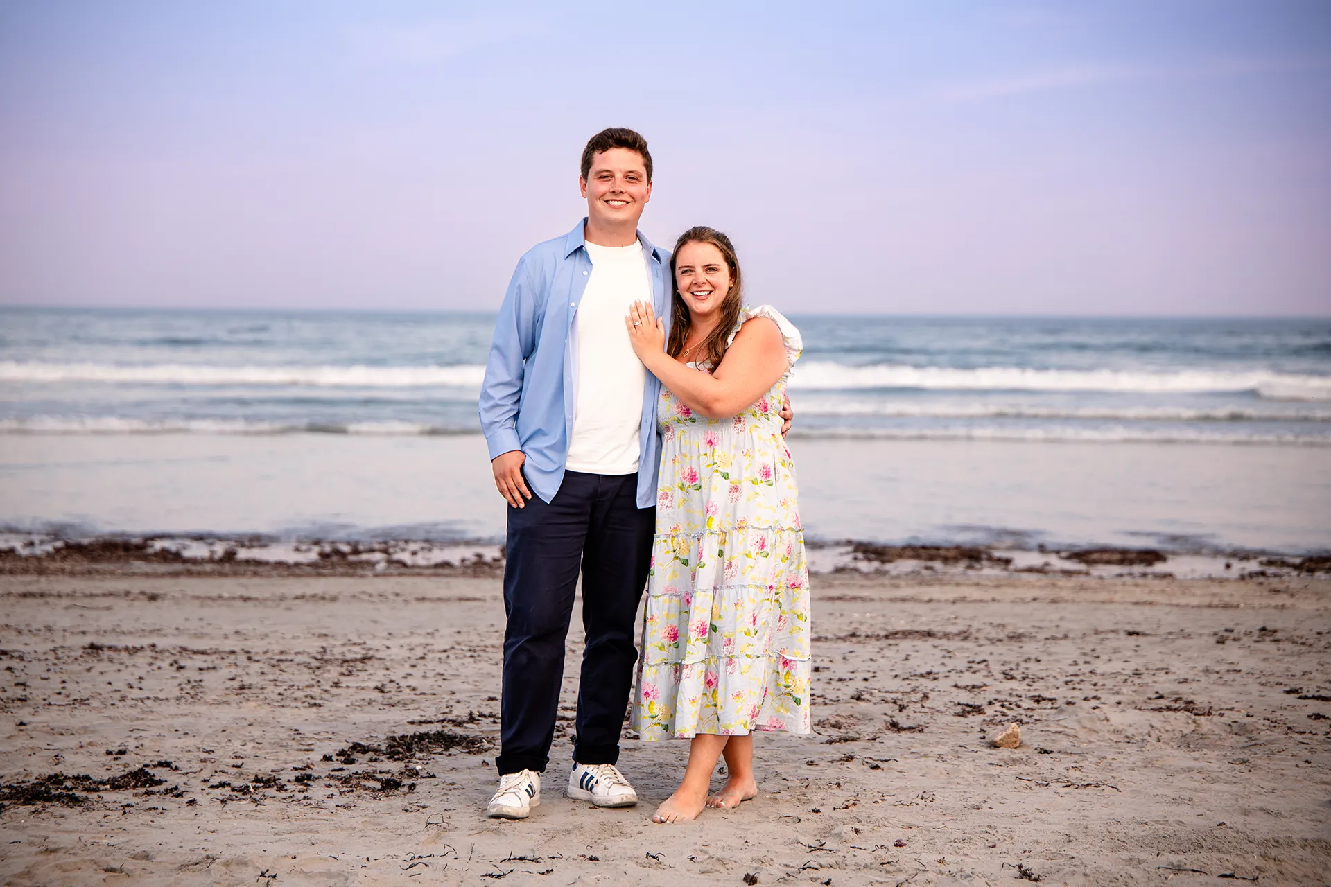 A newly engaged couple smile and pose during engagement portraits on Long Sands Beach in York, Maine.