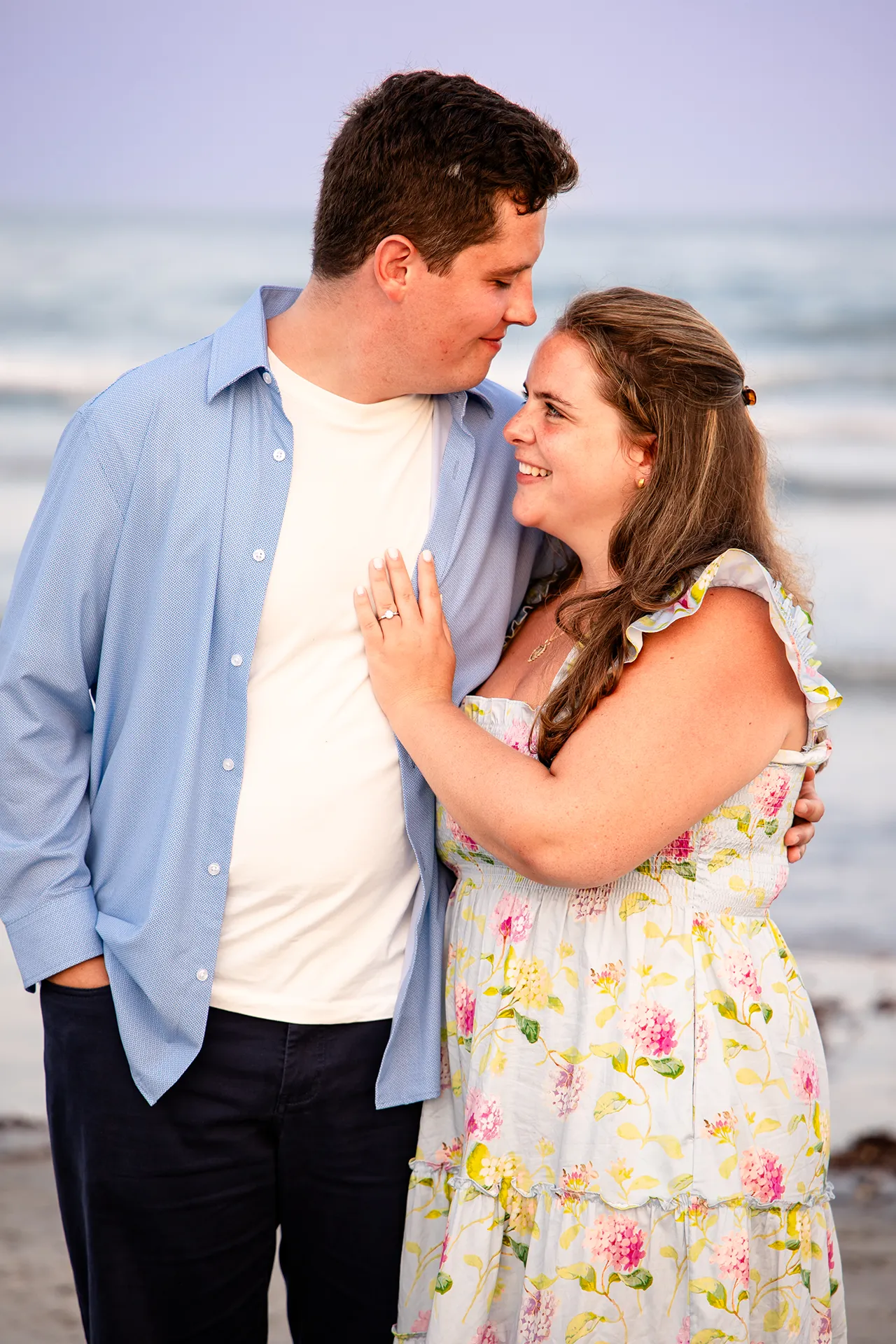A newly engaged couple smile at each other during engagement portraits on Long Sands Beach in York, Maine.