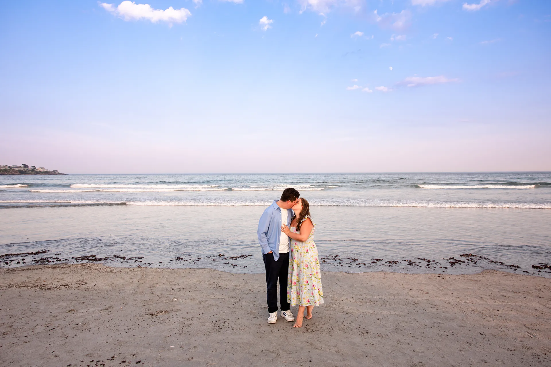 A newly engaged couple kiss on Long Sands Beach during engagement portraits in York, Maine.