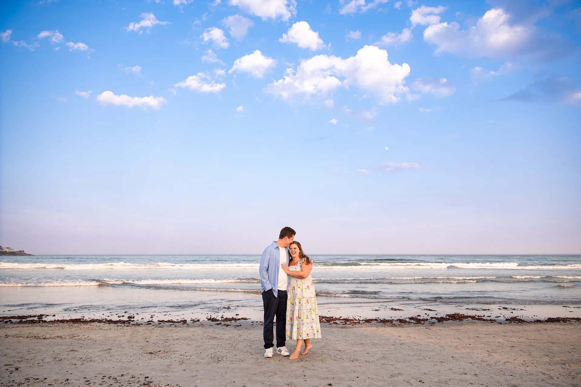 A man kisses a woman on the head during engagement portraits on Long Sands Beach in York, Maine.