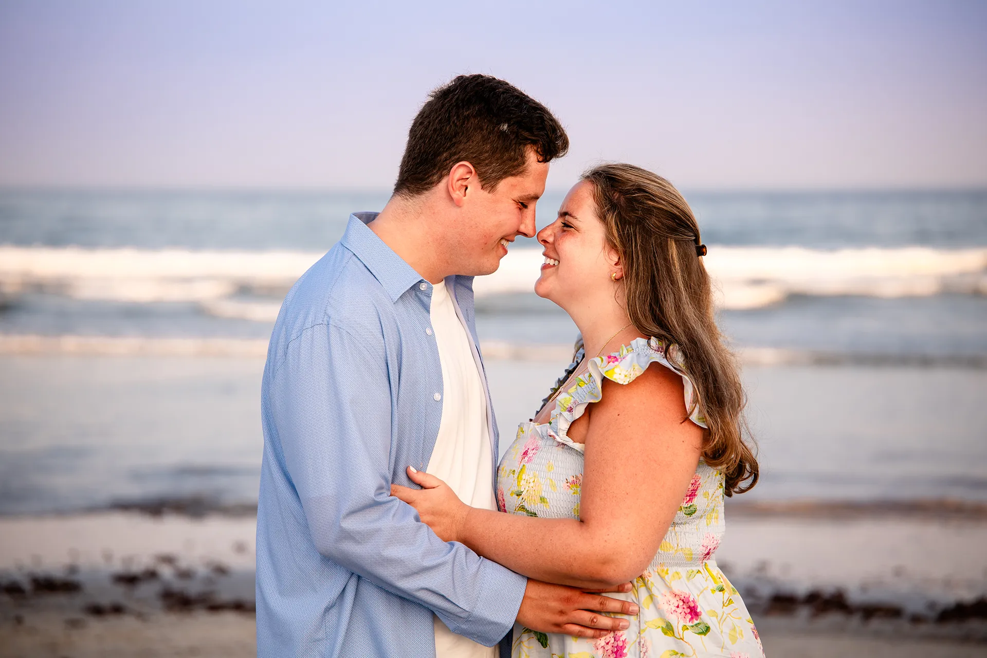 A man and woman rub noses and smile during engagement portraits on Long Sands Beach in York, Maine.