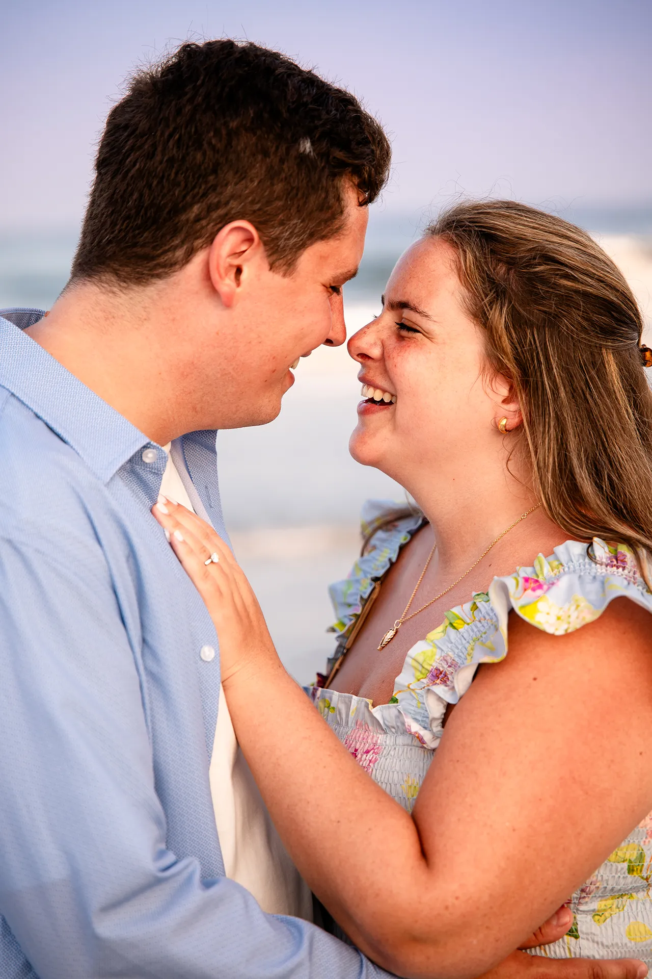 A newly engaged couple laugh as they rub noses during engagement portraits on Long Sands Beach in York, Maine.