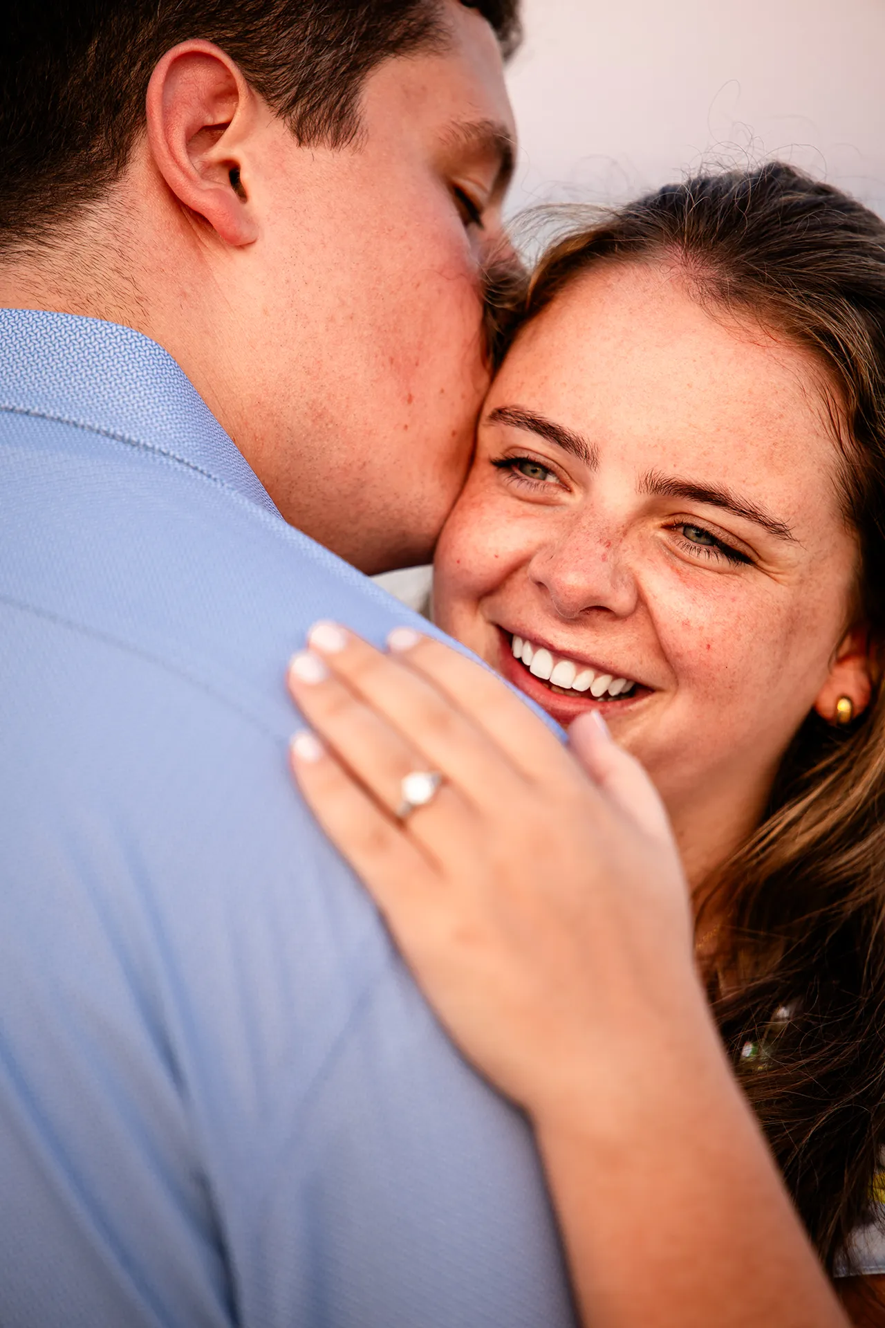 A woman smiles as a man kisses her on the cheek during engagement portraits on Long Sands Beach in York, Maine.