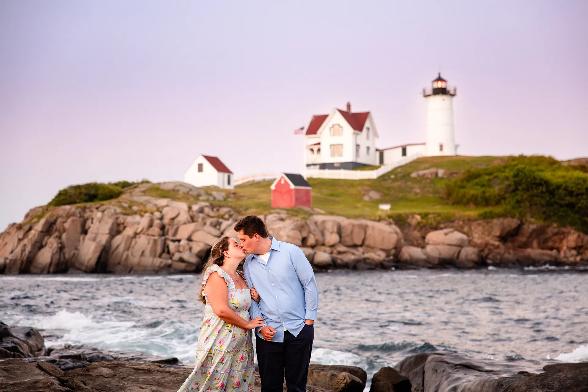 A man and woman kiss during sunset engagement portraits at Nubble Lighthouse in York, Maine.