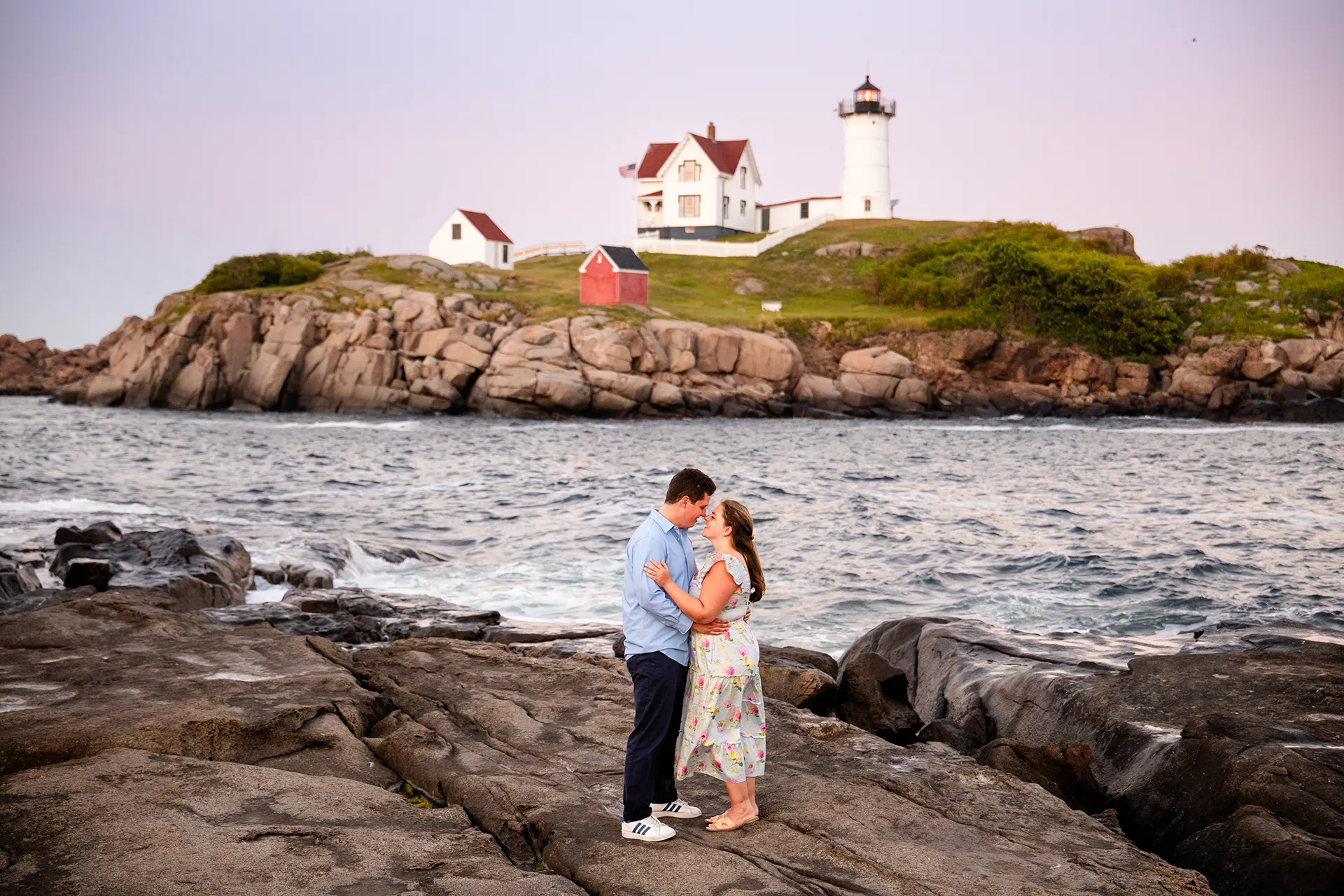 A man and woman rub noses during sunset engagement portraits at Nubble Lighthouse in York, Maine.