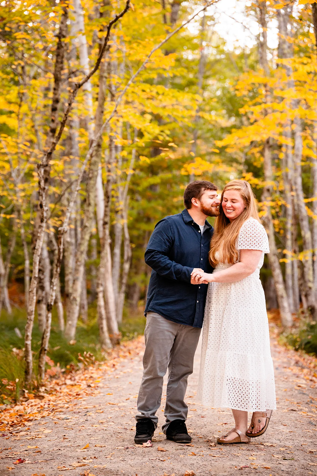 A man and woman hold hands and snuggle during a fall engagement session on the Hemlock Trail at Acadia National Park in Bar Harbor, Maine.