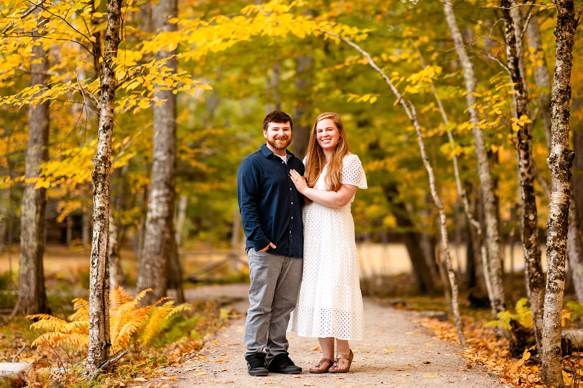A man and woman smile and pose during a fall engagement session near the Wild Gardens of Acadia at Acadia National Park in Bar Harbor, Maine.