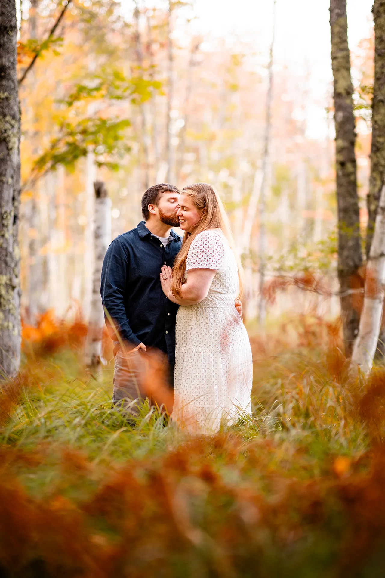 A man kissing a woman on the cheek while they pose in a field during an engagement session at Acadia National Park in Bar Harbor, Maine.