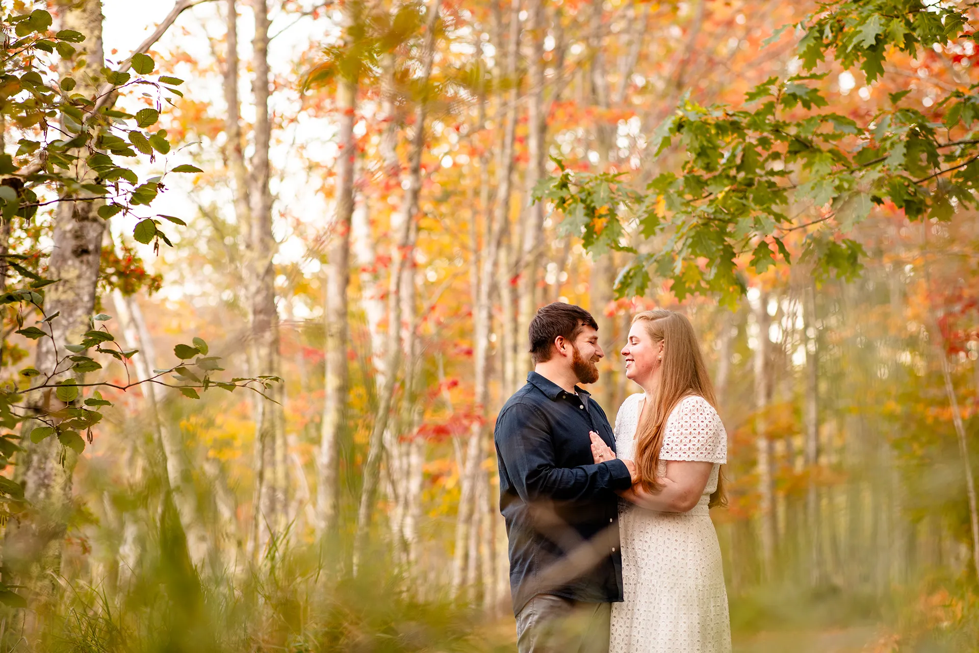 A man and woman smile at each other during a fall engagement session on the Hemlock Trail at Acadia National Park in Bar Harbor, Maine.