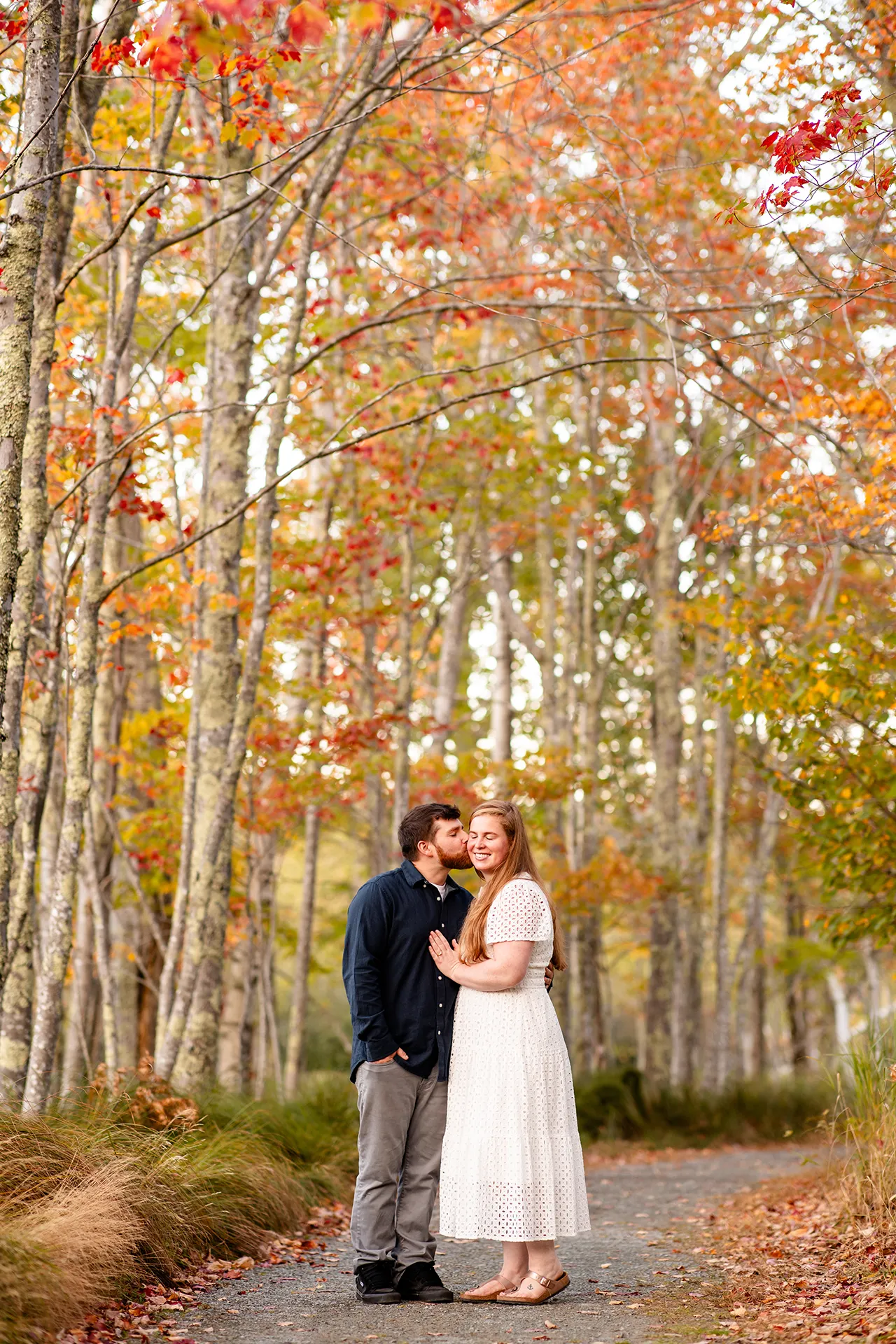 A woman is kissed on the cheek by a man during a fall engagement session near the Jesup Path at Acadia National Park in Bar Harbor, Maine.