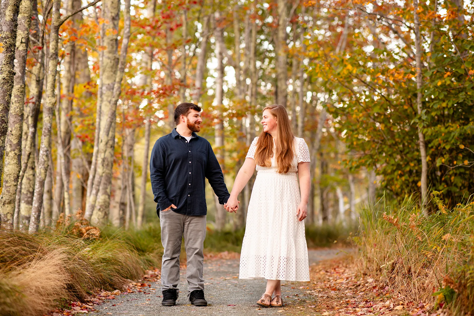 A man and woman hold hands and smile at each other during a fall engagement session at Acadia National Park in Bar Harbor, Maine.