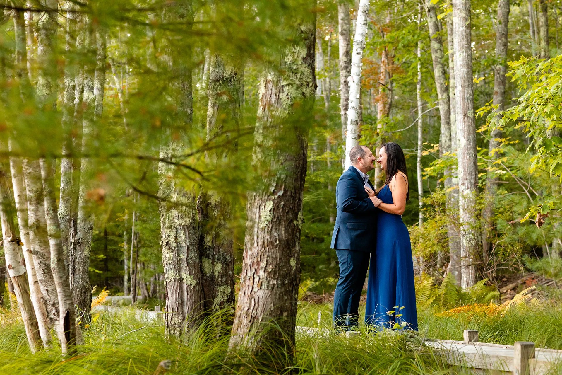 An engaged couple smile at each other during a engagement session on the Jesup Path in Acadia National Park, Maine.