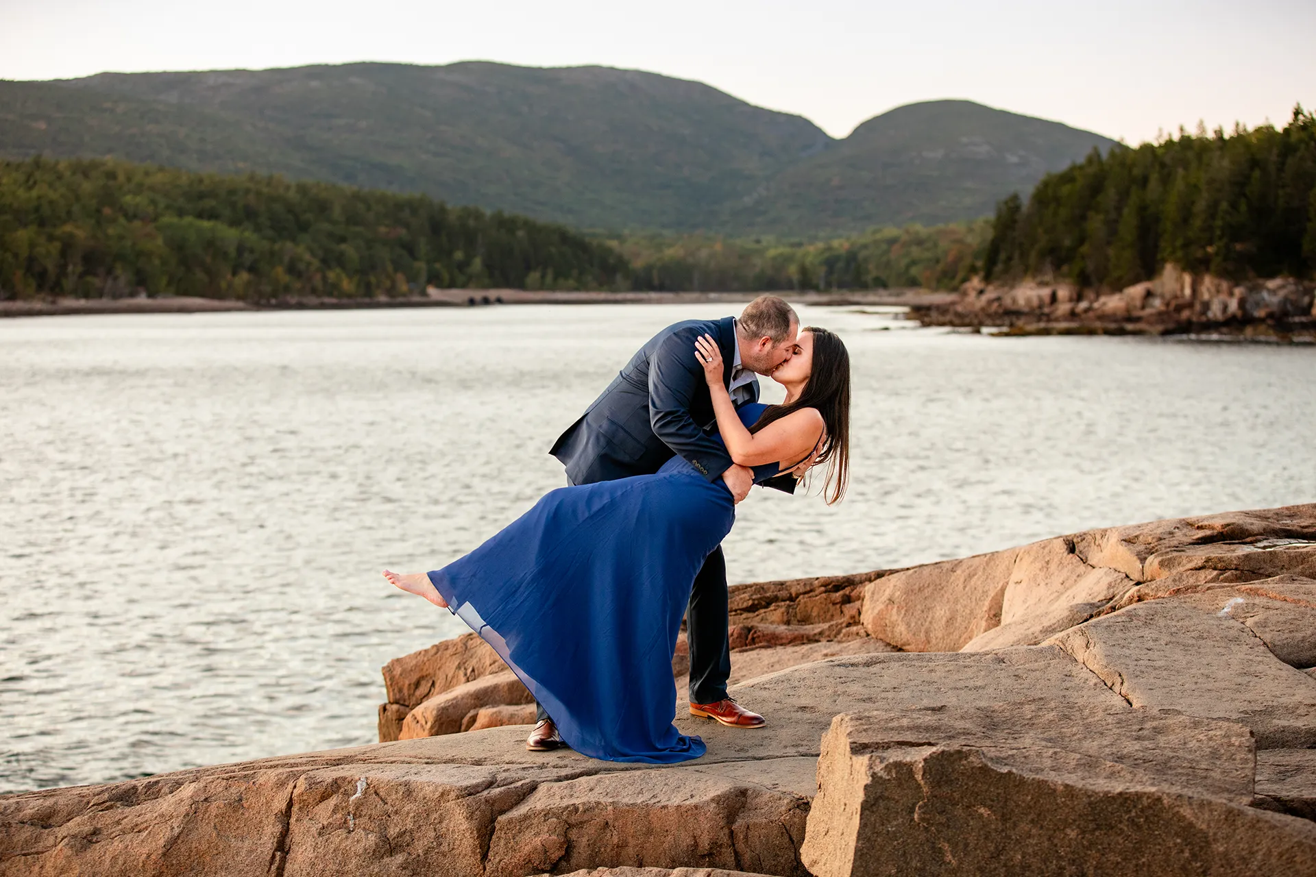An engaged couple kiss as they dip during an engagement session on Otter Point in Acadia National Park near Bar Harbor, Maine.