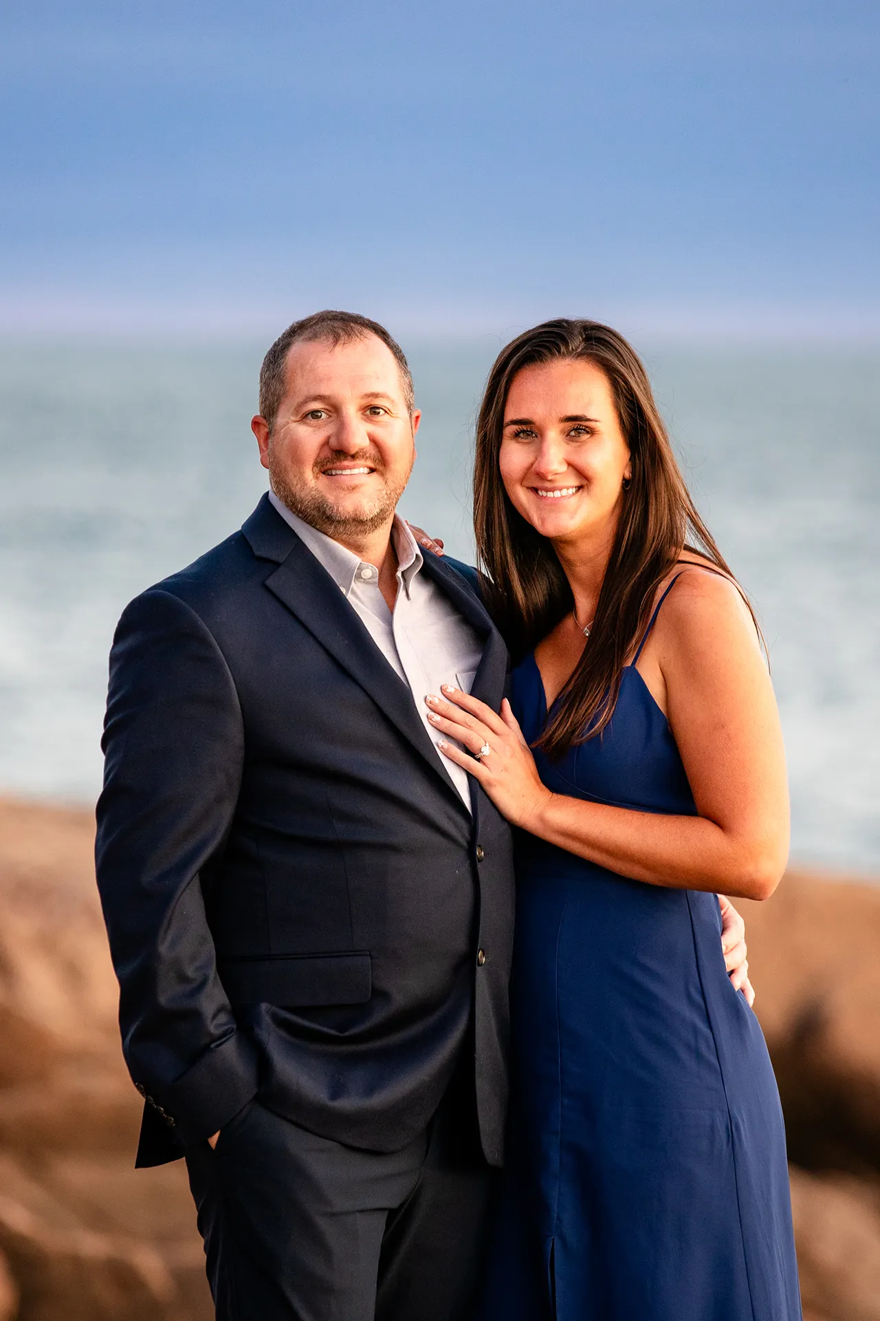 An engaged couple smile and pose during an engagement session on Otter Point in Acadia National Park near Bar Harbor, Maine.