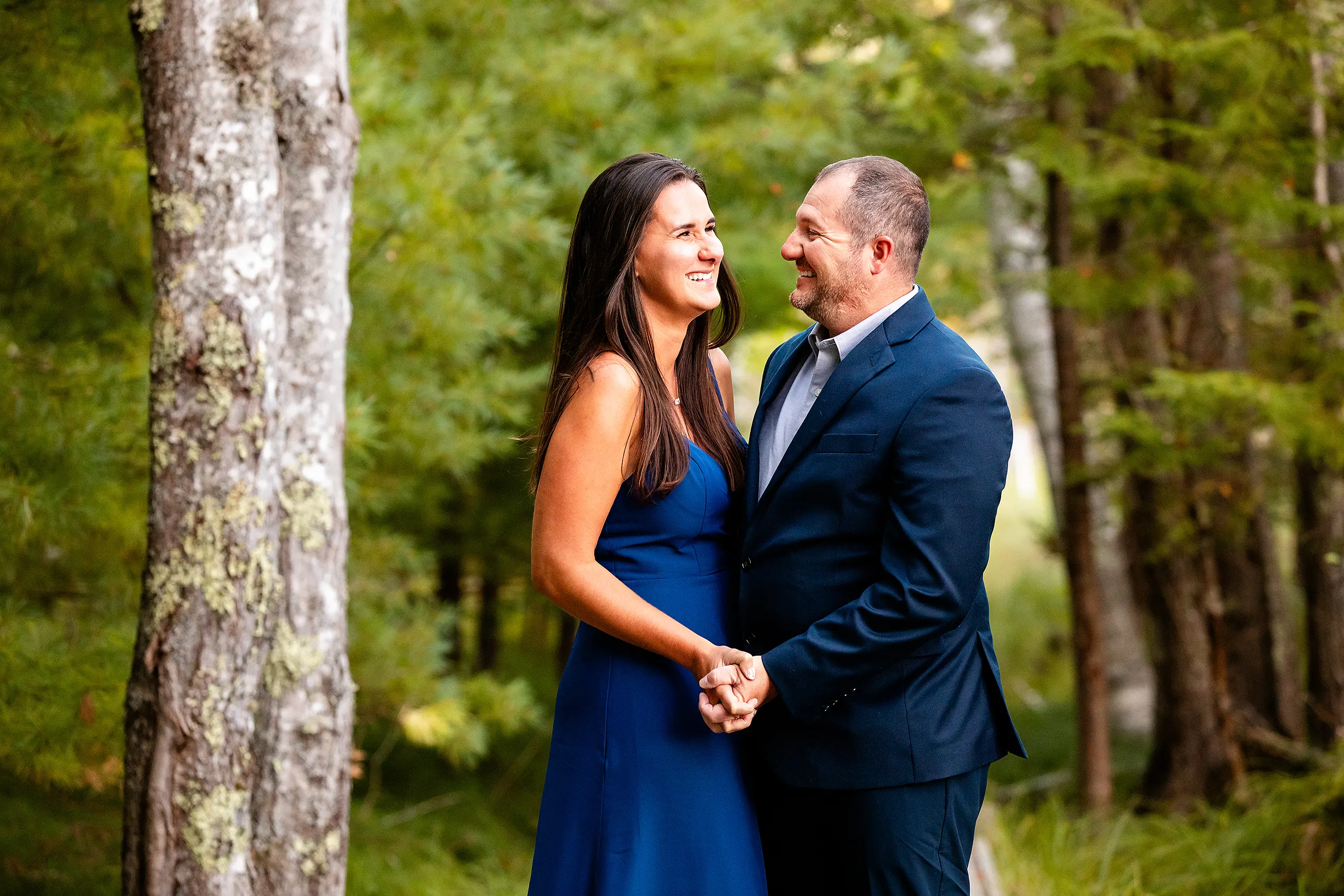 An engaged couple hold hands and laugh during a engagement session on the Jesup Path in Acadia National Park, Maine.