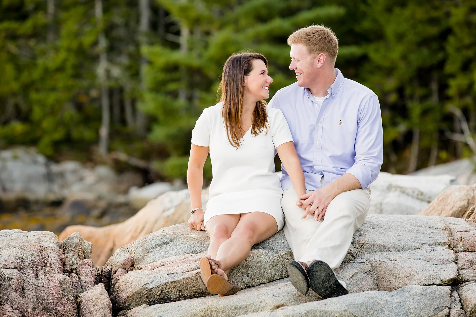 maine engagement photography stephanie nick 02 A man and woman sit on a rock and smile at each other during an engagement session at Curtis Cove in Blue Hill, Maine.