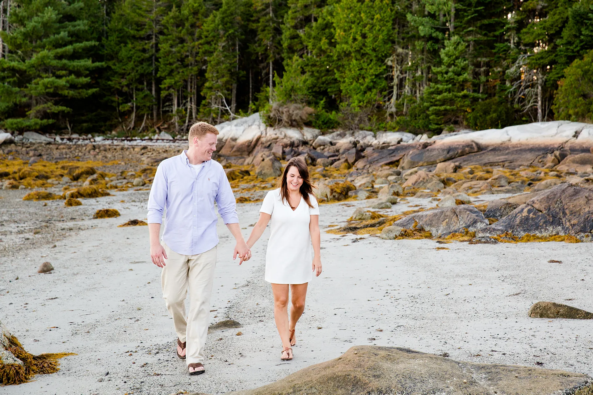 maine engagement photography stephanie nick 06 An engaged couple smiles as they walk on a beach during an engagement session at Curtis Cove in Blue Hill, Maine.