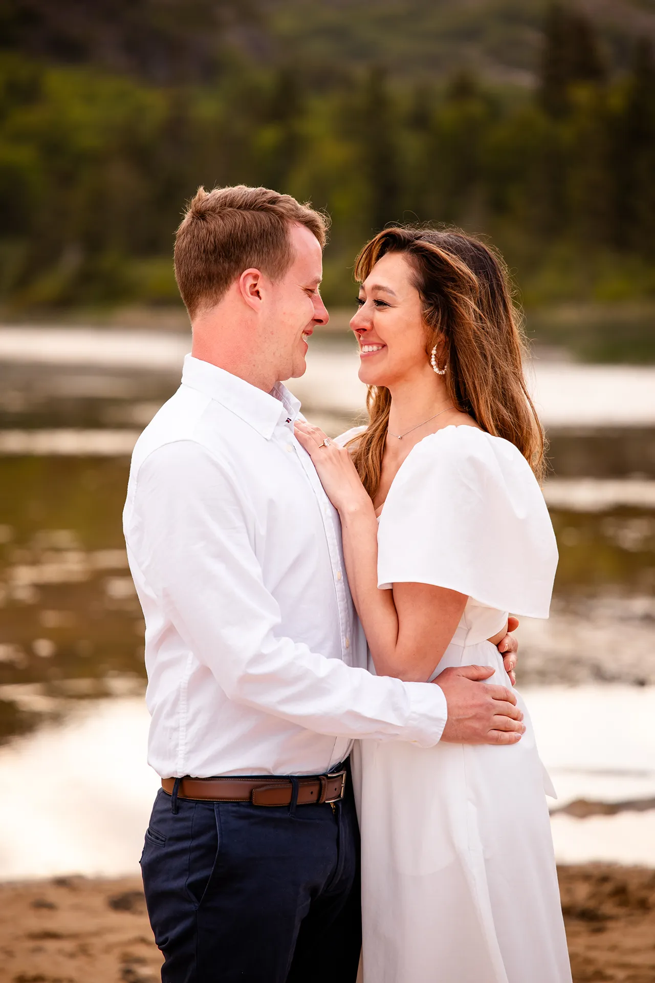 An engaged couple smile at each other during a portrait session at Sand Beach in Acadia National Park near Bar Harbor, Maine.