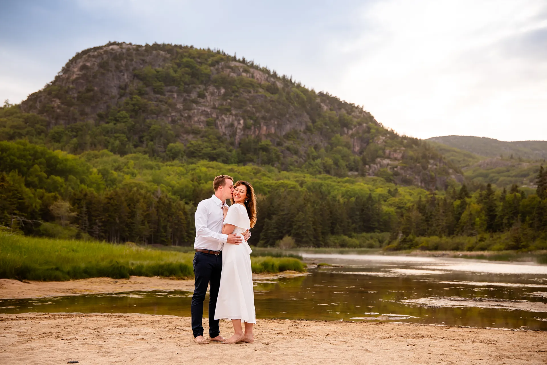 A man kisses a woman on the cheek during an engagement session in front of Beehive Mountain in Acadia National Park near Bar Harbor, Maine.