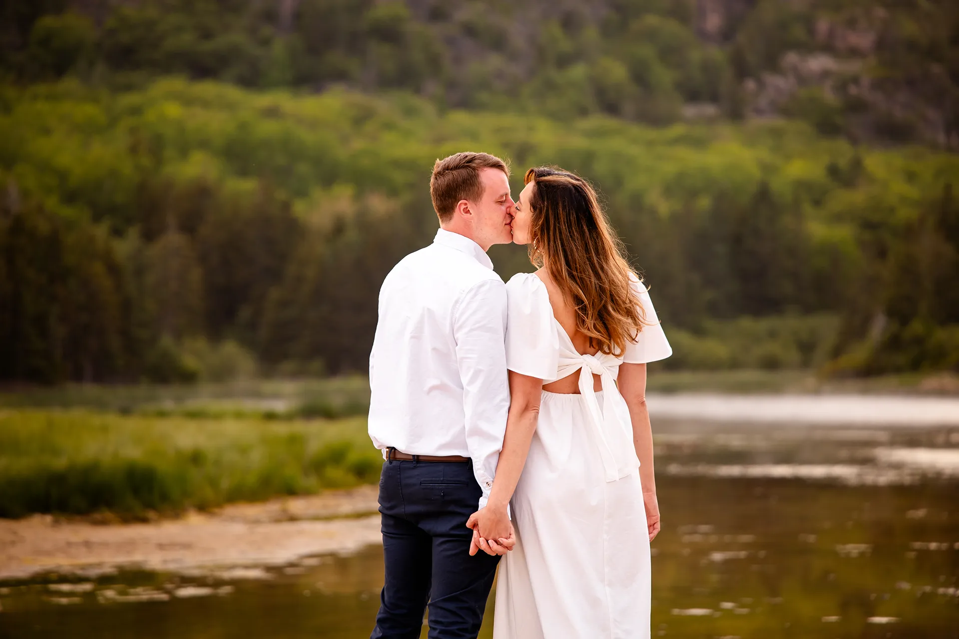 A man and woman hold hands and kiss during an engagement session at Sand Beach in Acadia National Park near Bar Harbor, Maine.