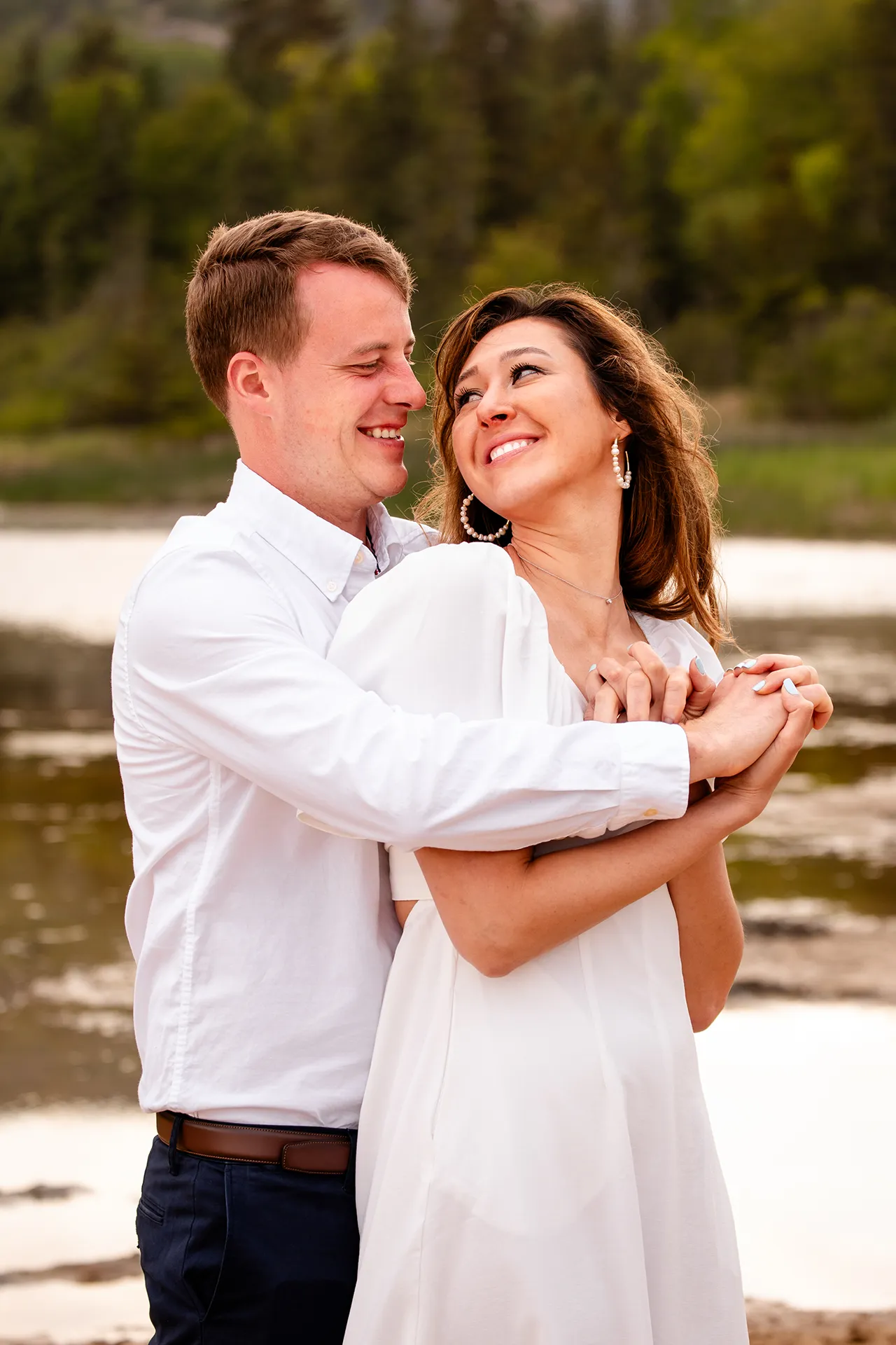 A man hugs a smiling woman during an engagement session at Sand Beach in Acadia National Park near Bar Harbor, Maine.
