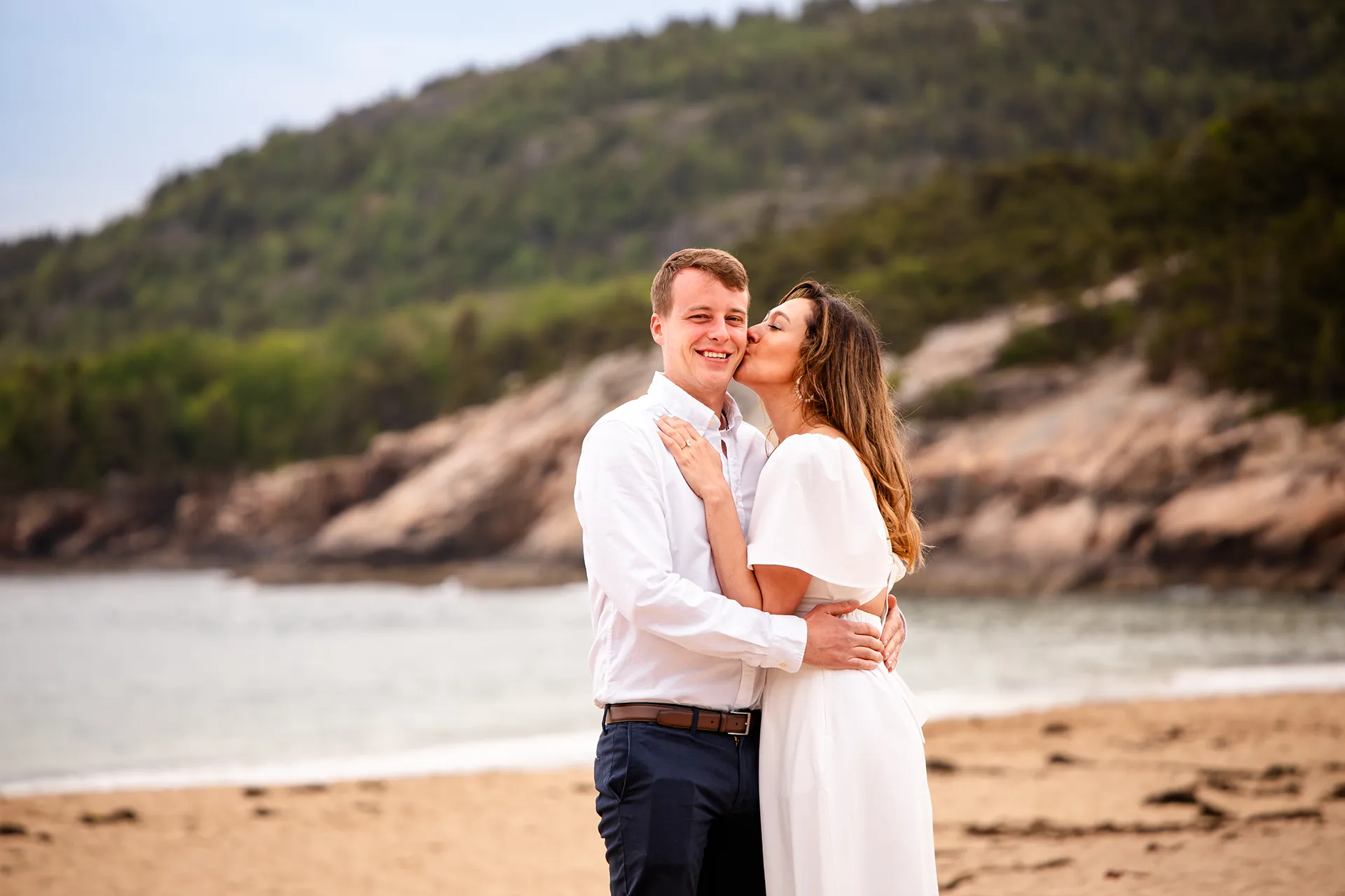 A woman kisses a man on the cheek during an engagement session at Sand Beach in Acadia National Park near Bar Harbor, Maine.