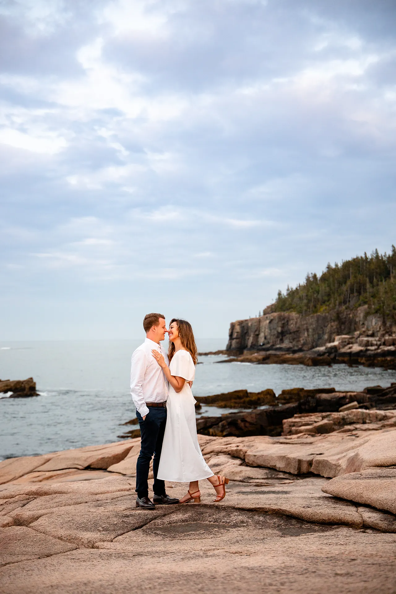 A man and woman rub noses during a coastal engagement session near Otter Cliff in Acadia National Park near Bar Harbor, Maine.