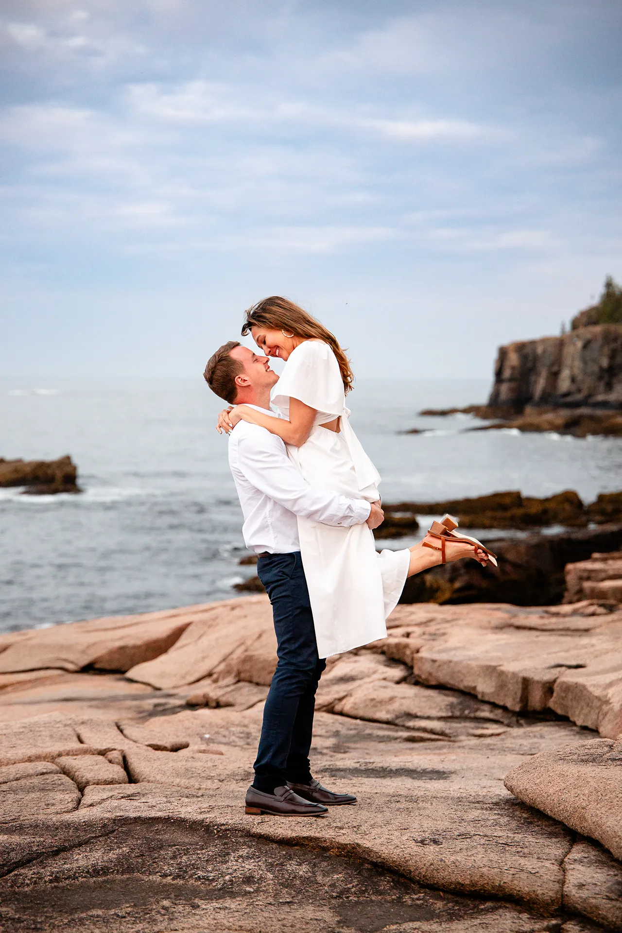 A woman smiles as a man lifts her in the air during a portrait session near Otter Cliff in Acadia National Park near Bar Harbor, Maine.