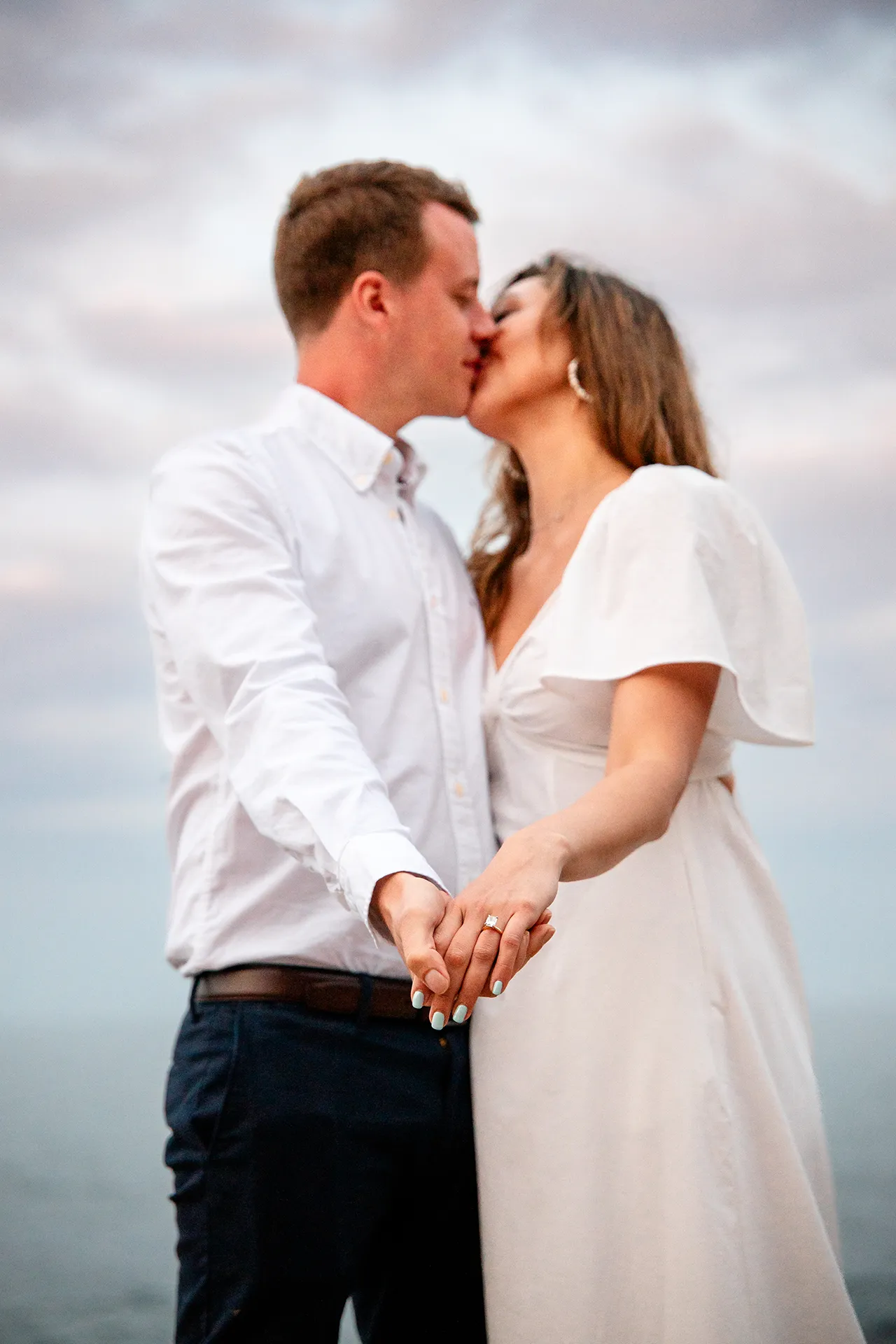 An engaged couple kiss as they hold hands during a portrait session near Otter Cliff in Acadia National Park near Bar Harbor, Maine.