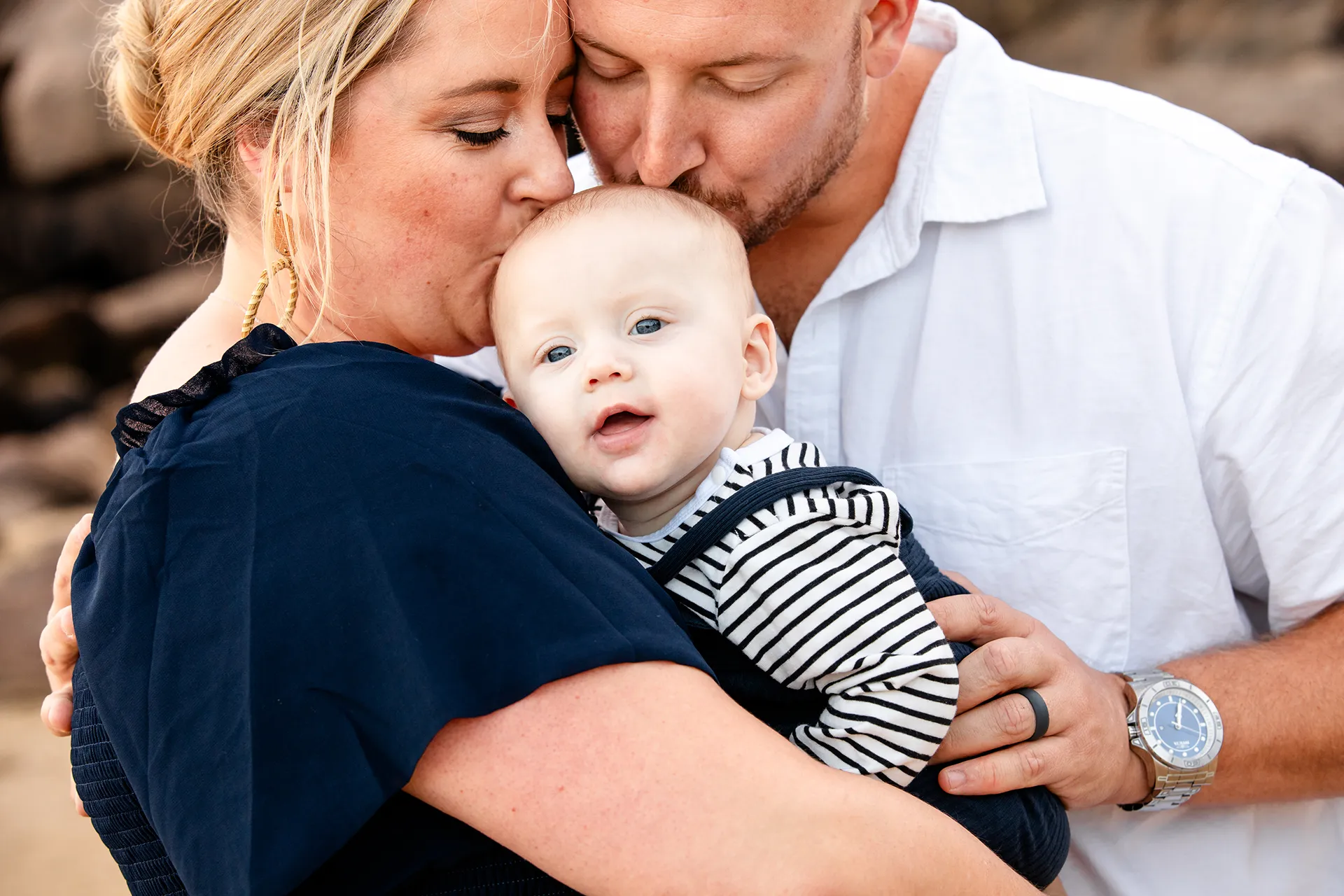 maine family photography daehler 03 A mom and dad kiss their son's head during a family portrait session on Sand Beach in Acadia National Park near Bar Harbor, Maine.