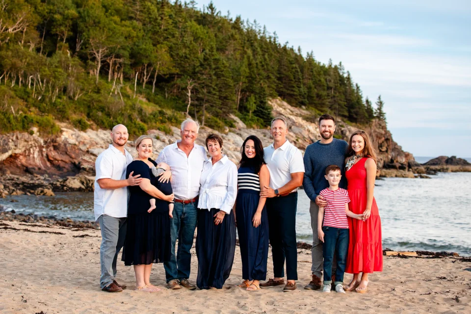 An extended family smile and pose during a family portrait session on Sand Beach in Acadia National Park near Bar Harbor, Maine.