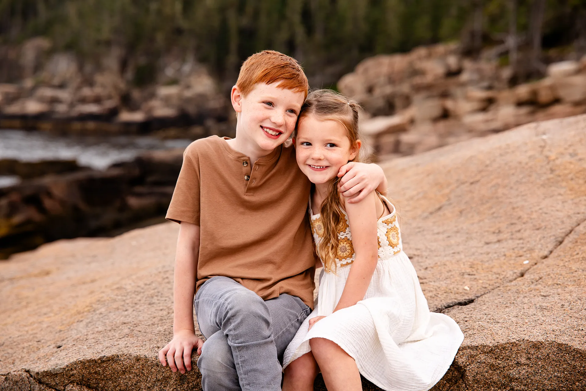 A boy has his arm around a girl as they sit and pose for family portraits at Acadia National Park in Bar Harbor, Maine.