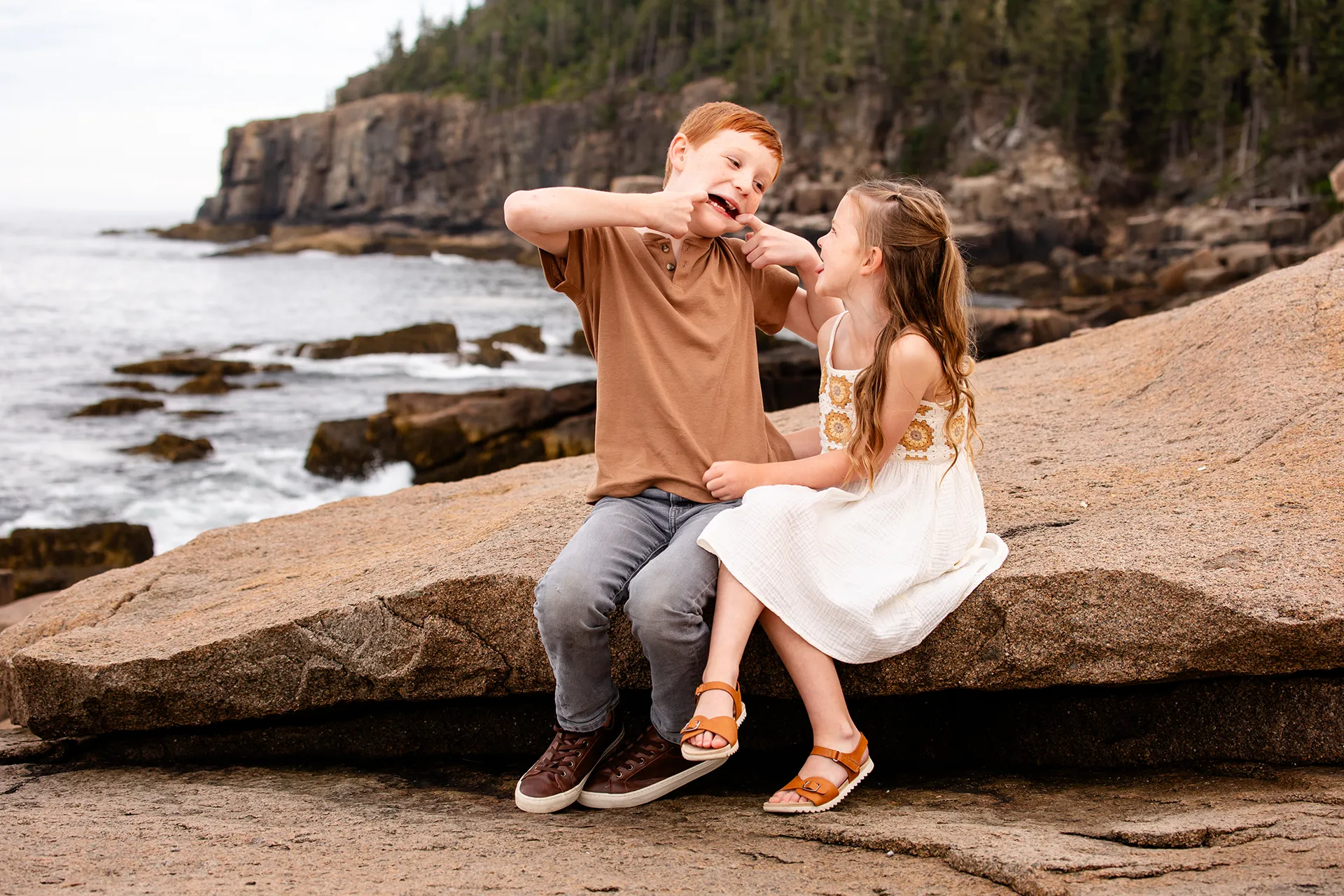 A boy and girl make faces at each other during family portraits near Otter Cliff in Acadia National Park in Bar Harbor, Maine.