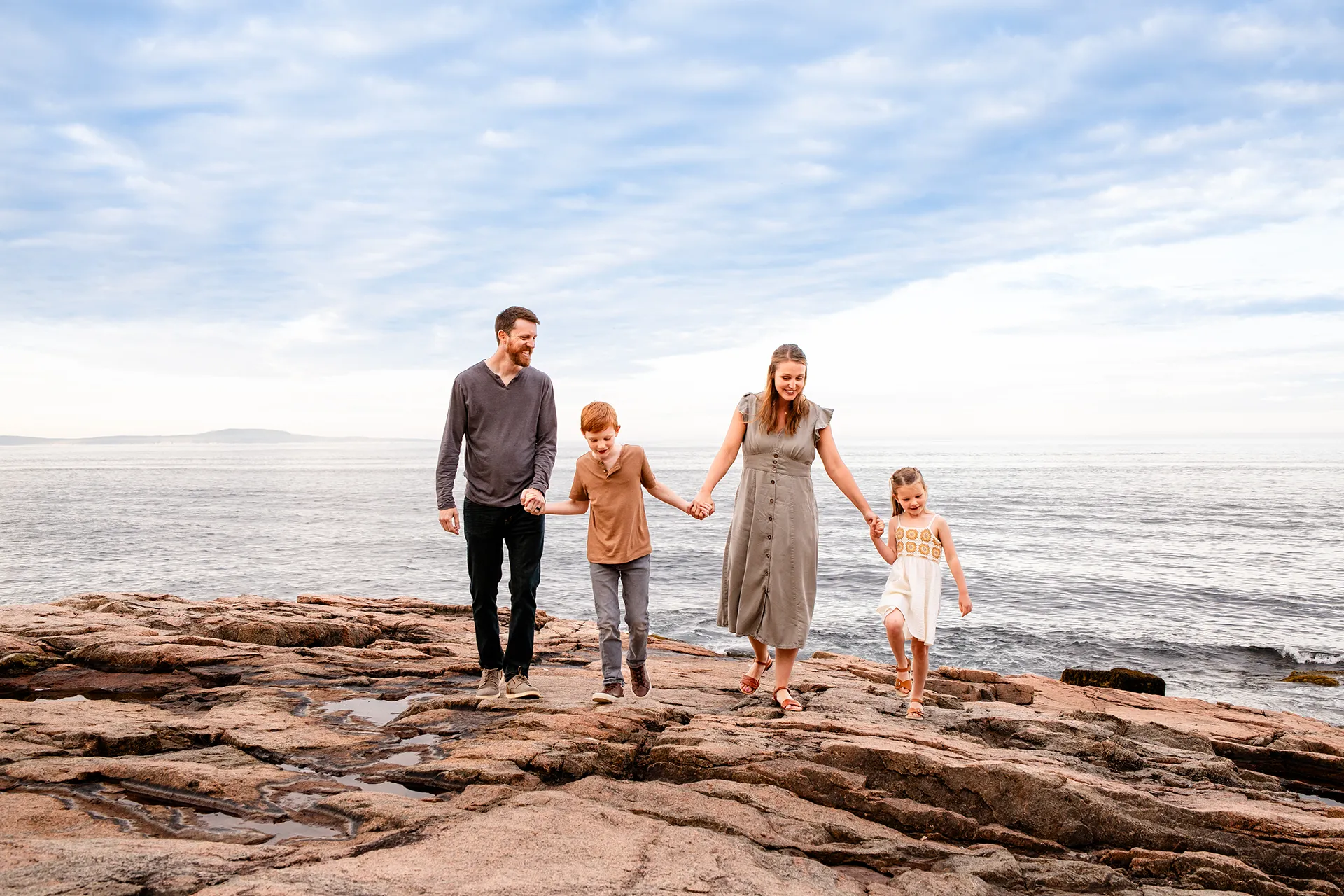 A mom and dad hold their son and daughter's hand as they walk during family portraits at Acadia National Park in Bar Harbor, Maine.