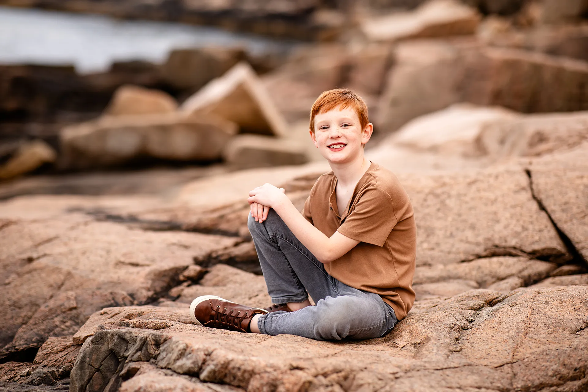 A boy sits and poses on a rock during family portraits near the Ocean Path in Acadia National Park in Bar Harbor, Maine.