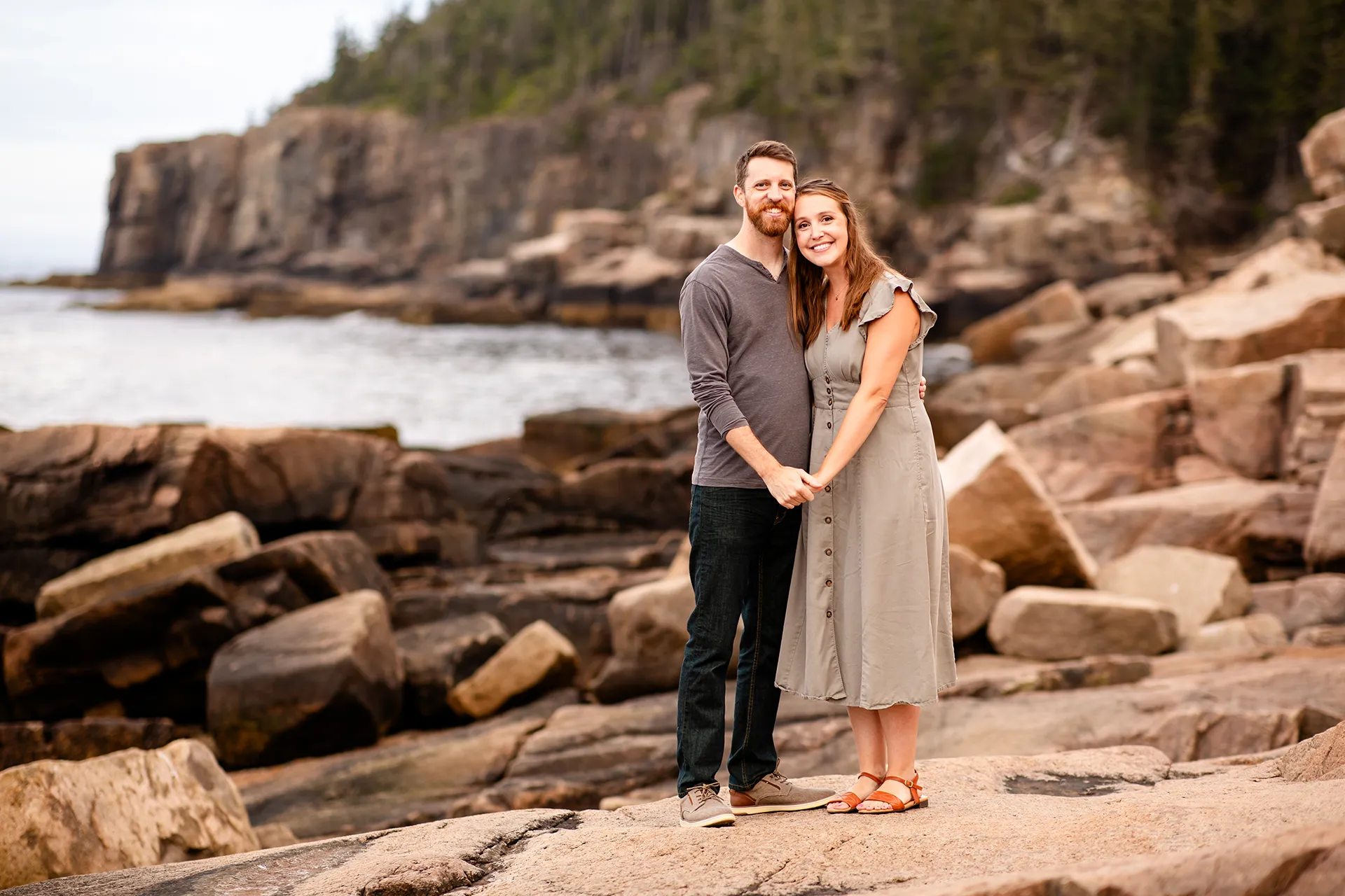 A man and woman smile and pose during family portraits near Otter Cliff at Acadia National Park in Bar Harbor, Maine.