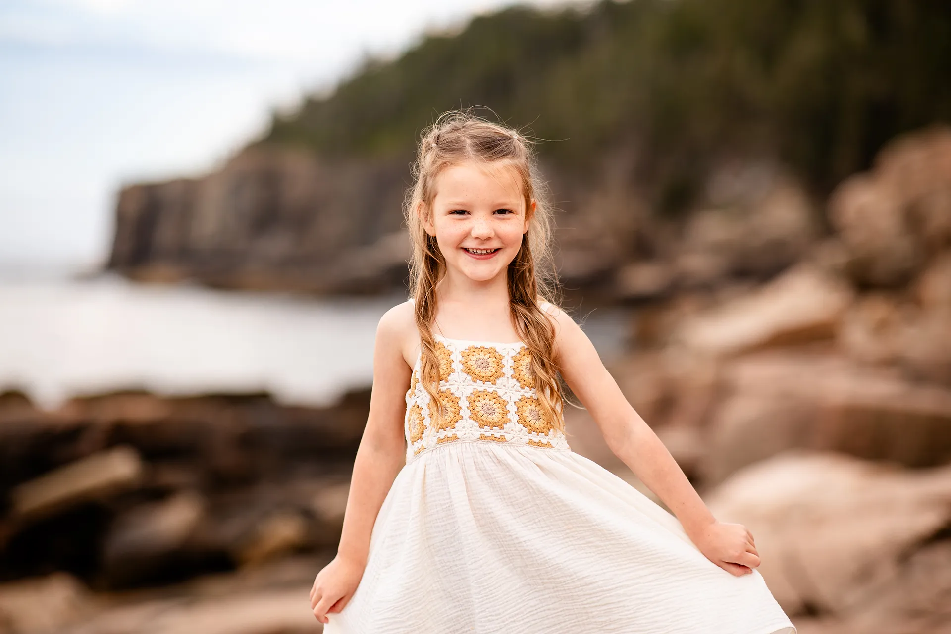 A girl smiles and poses during family portraits near Otter Cliff at Acadia National Park in Bar Harbor, Maine.