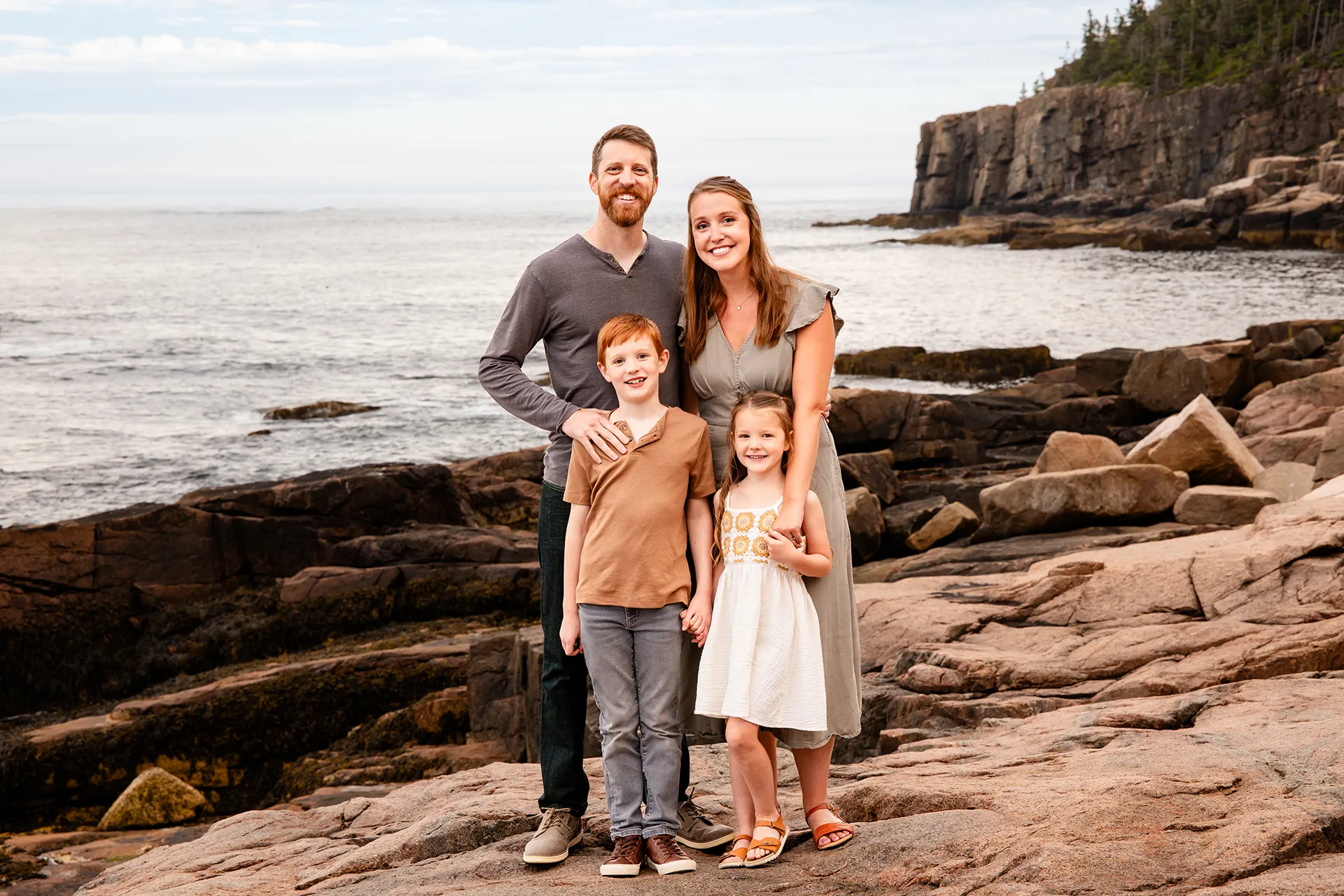 A family smiles and poses near the Ocean Path during family portraits at Acadia National Park in Bar Harbor, Maine.