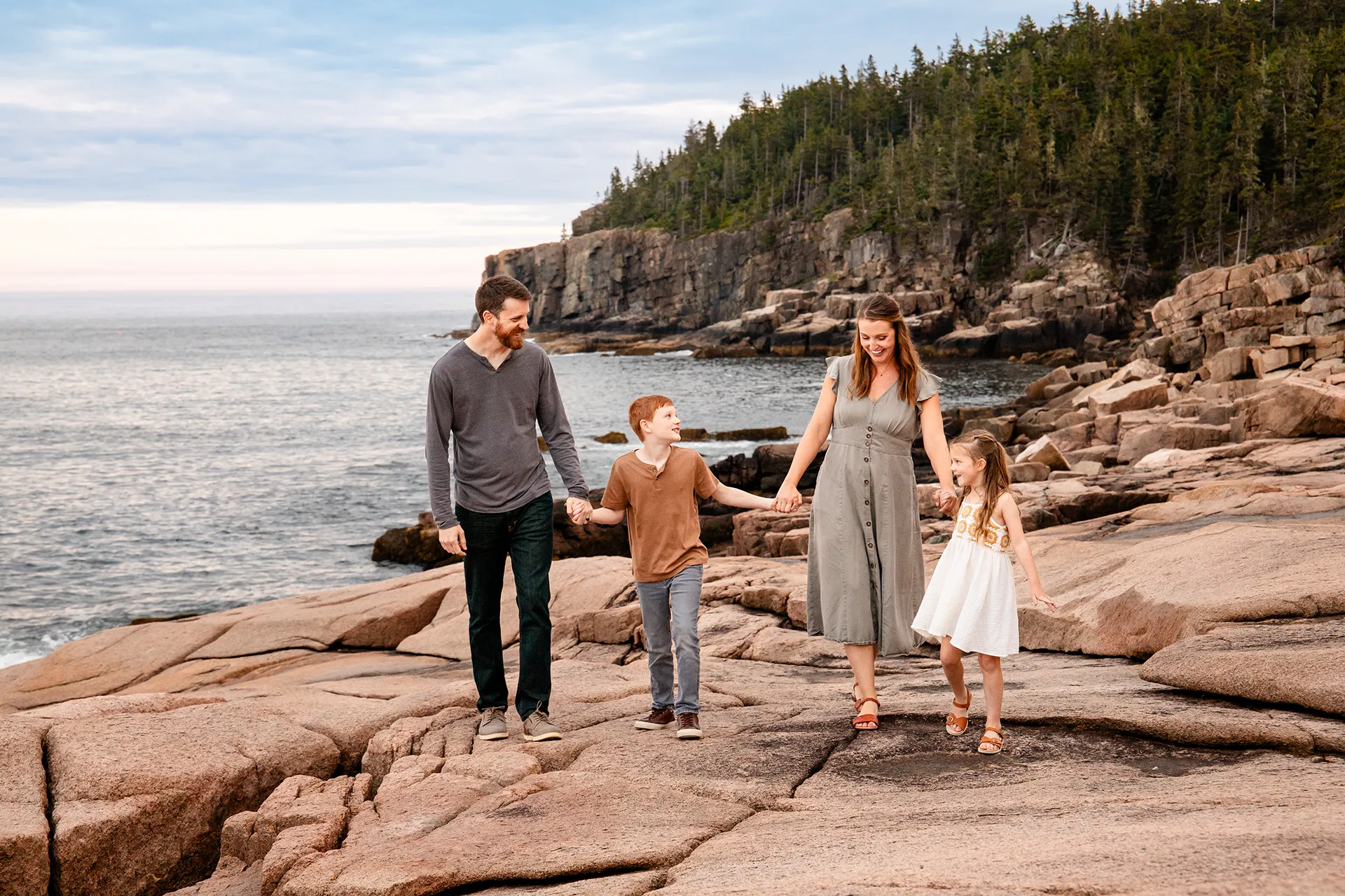A family holds hands and walks along the rocky coastline near Otter Cliff at Acadia National Park in Bar Harbor, Maine.