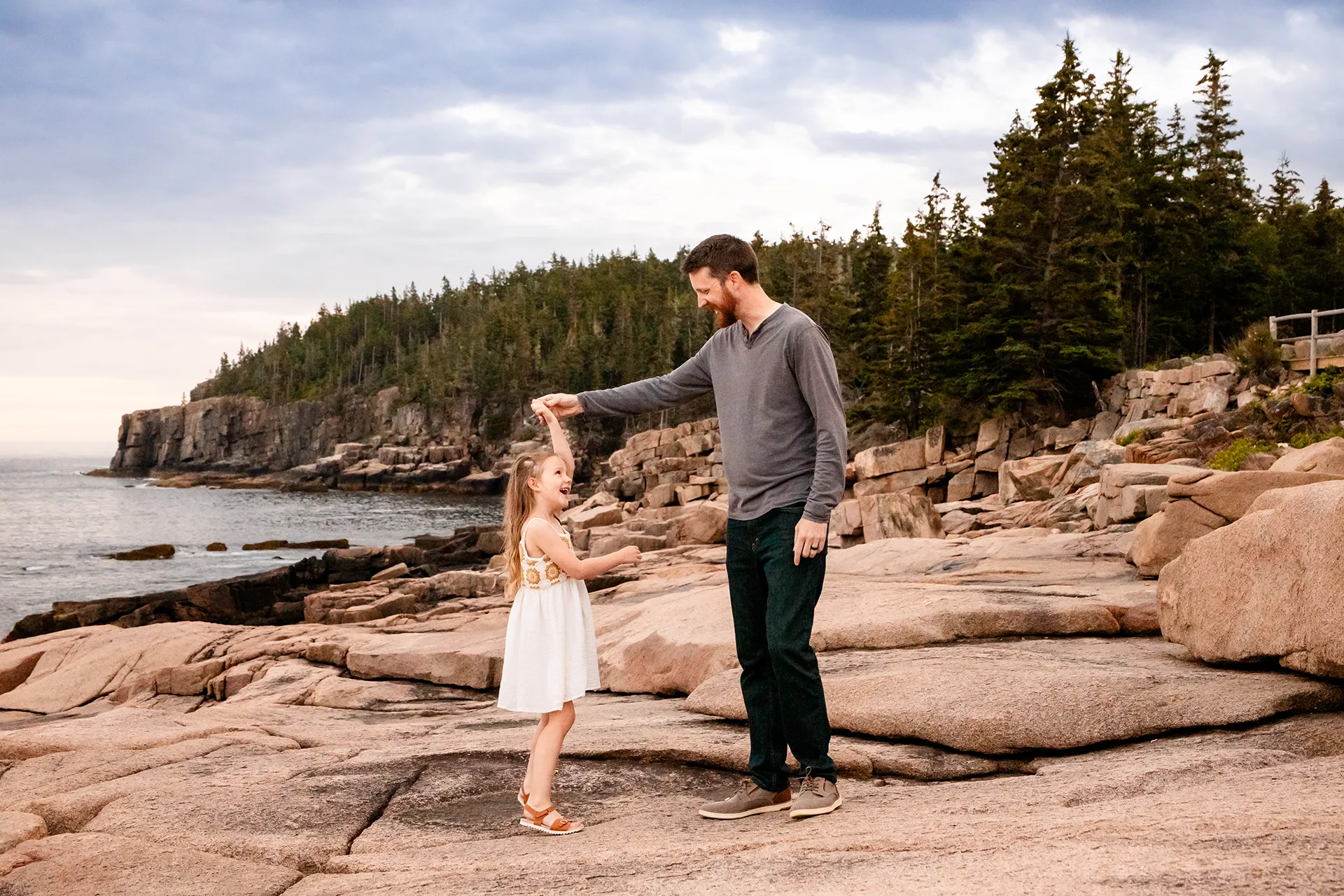 A dad spins his daughter as she laughs near Otter Cliff during family portraits at Acadia National Park in Bar Harbor, Maine.