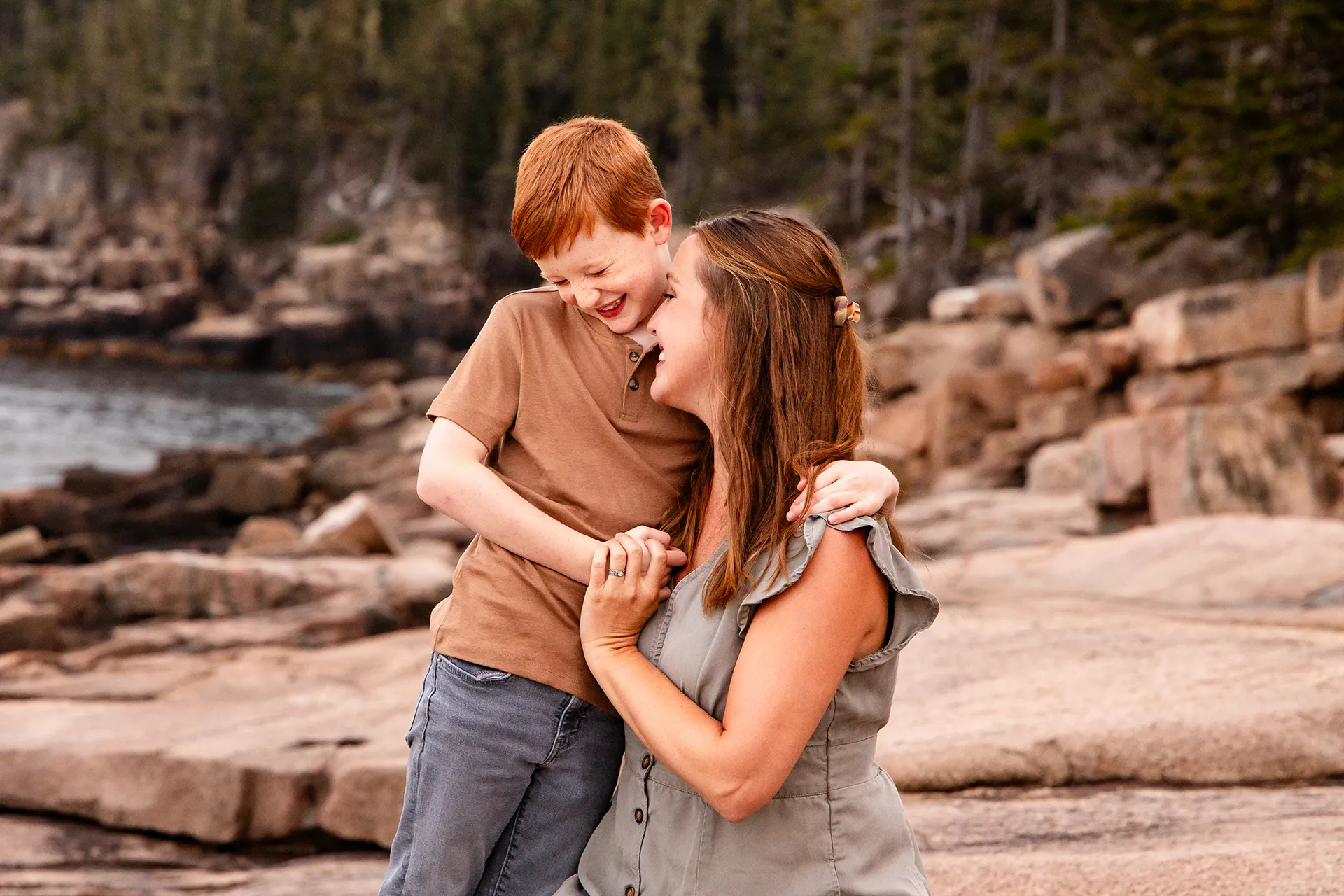 A mom and son snuggle together during family portraits near Ocean Path at Acadia National Park in Bar Harbor, Maine.