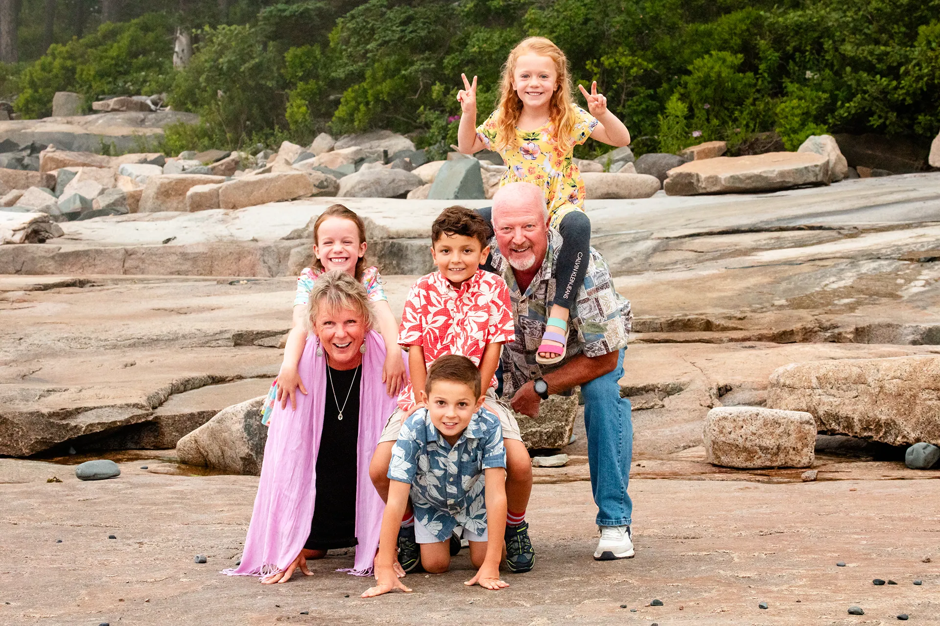 Grandchild sit on their grandparents backs while they pose for family portraits at Grindstone Point in Winter Harbor, Maine.
