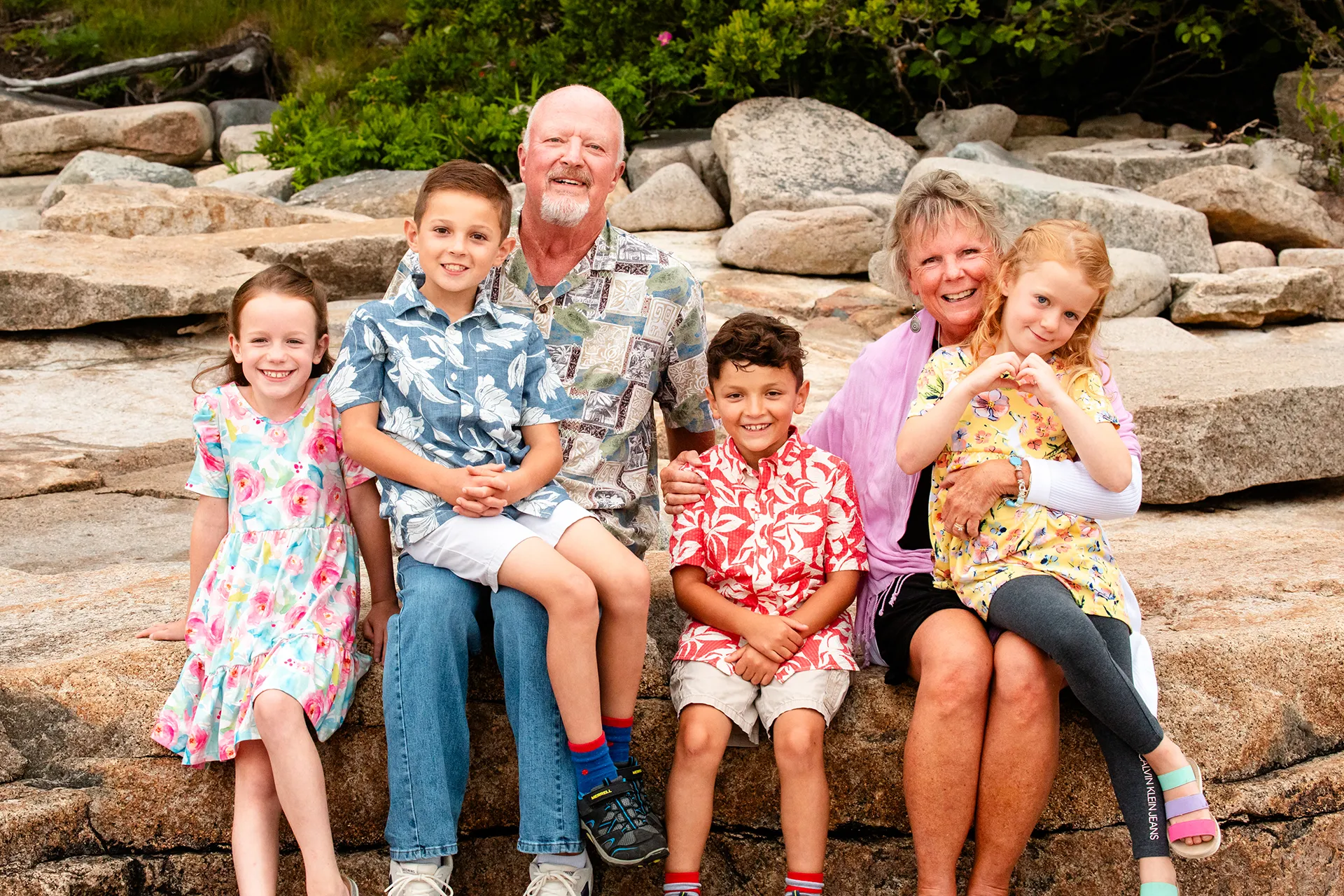Grandparents sit with their grandchildren while they smile an pose for family portraits at Grindstone Point in Winter Harbor, Maine.