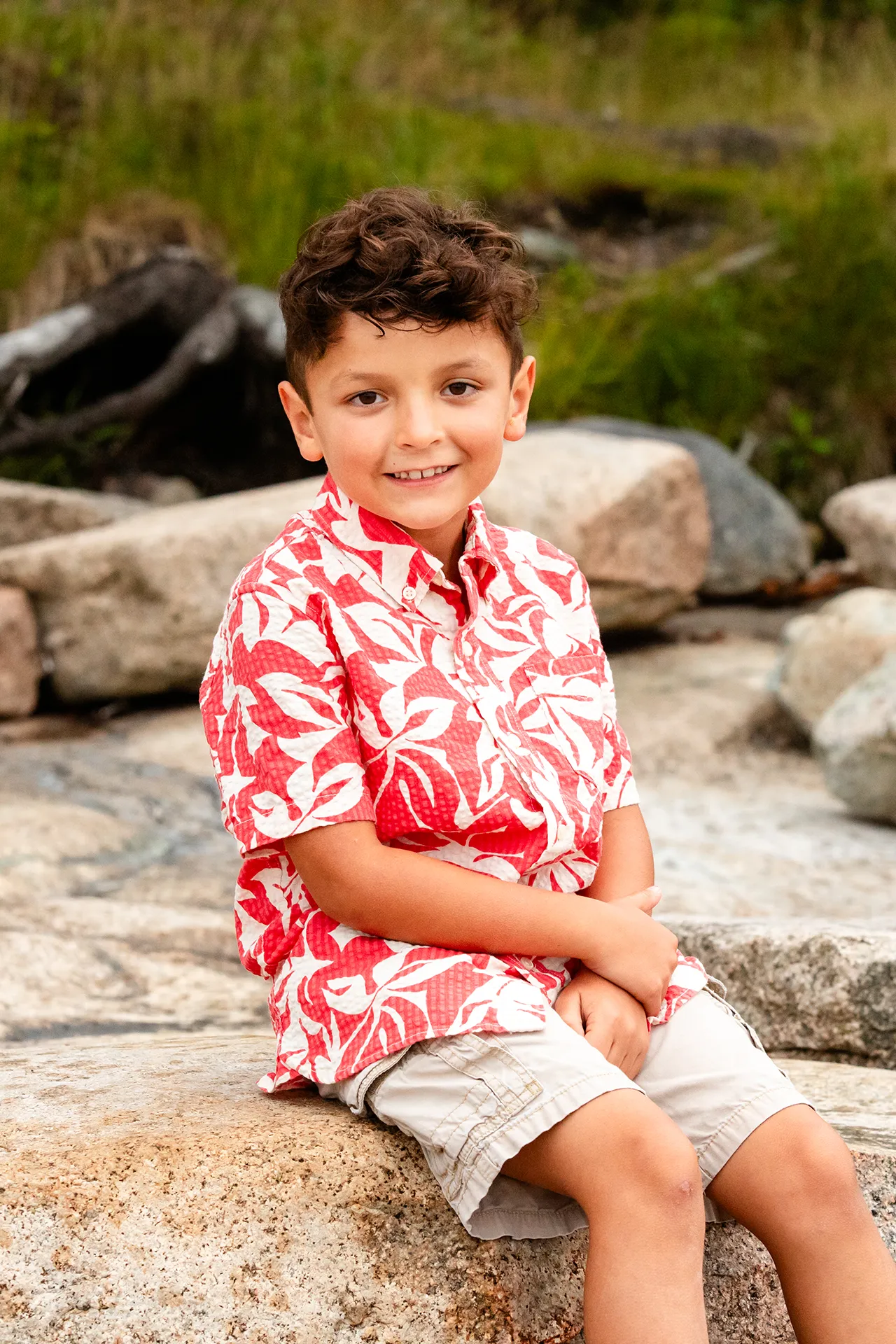 A boy sits and smiles for portraits during a family session at Grindstone Point in Winter Harbor, Maine.