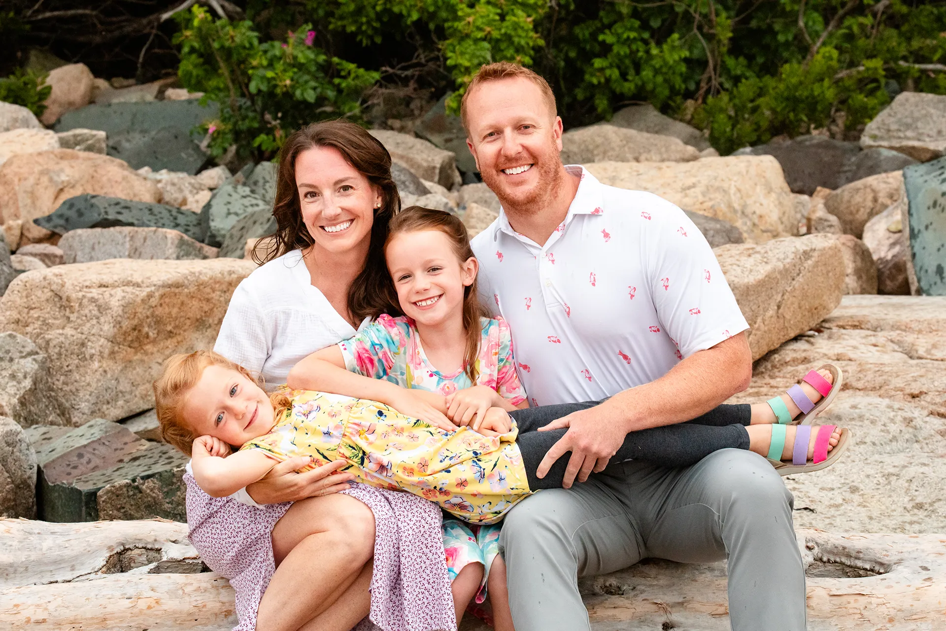 A girl lays across her parents and sister's laps during family portraits at Grindstone Point in Winter Harbor, Maine.