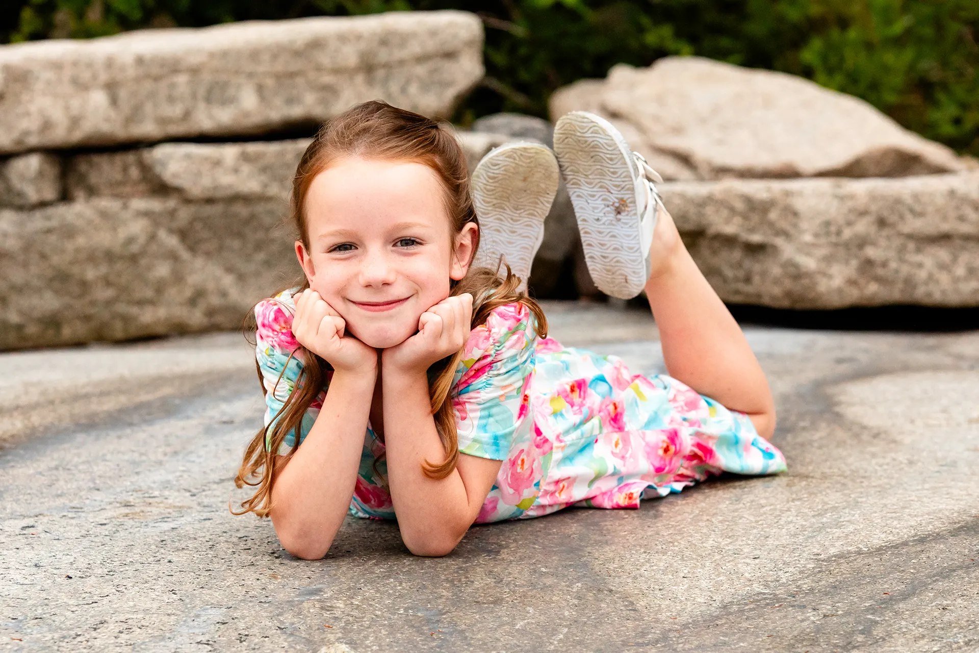 A girl lays on her belly and poses during family portraits at Grindstone Point in Winter Harbor, Maine.